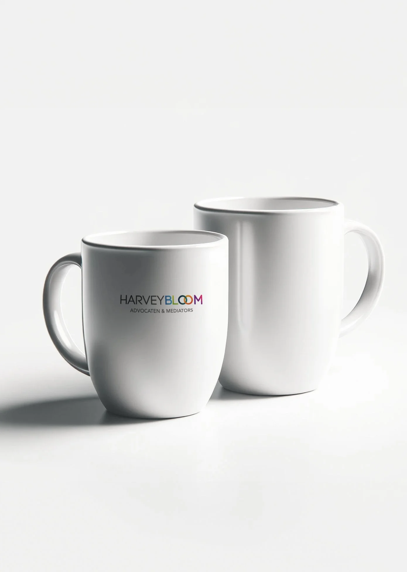 Twee witte koffie- of theekruiken, één met het logo van Harvey Bloom Advocaten & Mediators, op een witte achtergrond.