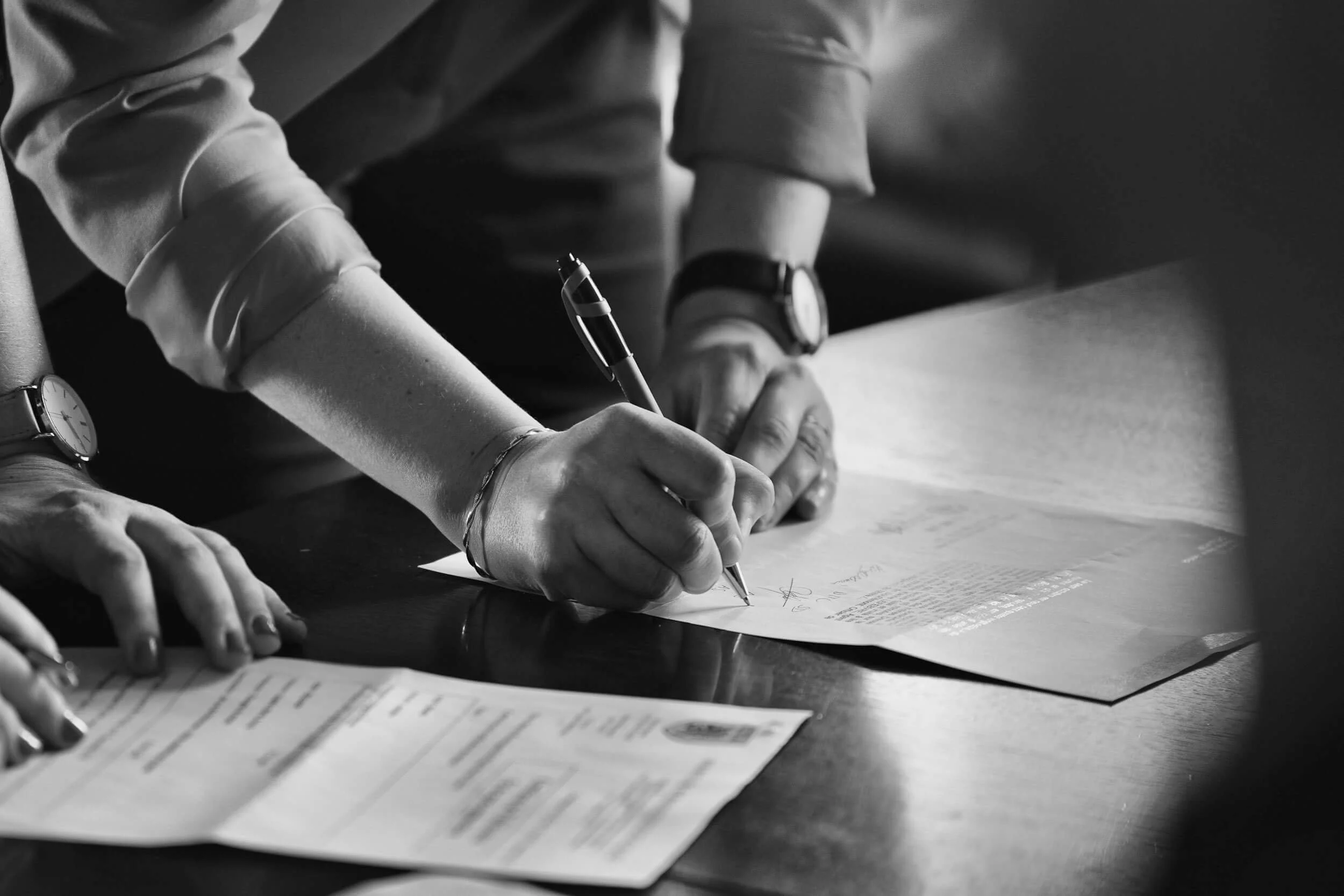 Mensen ondertekenen documenten op een tafel, zwart-wit foto.