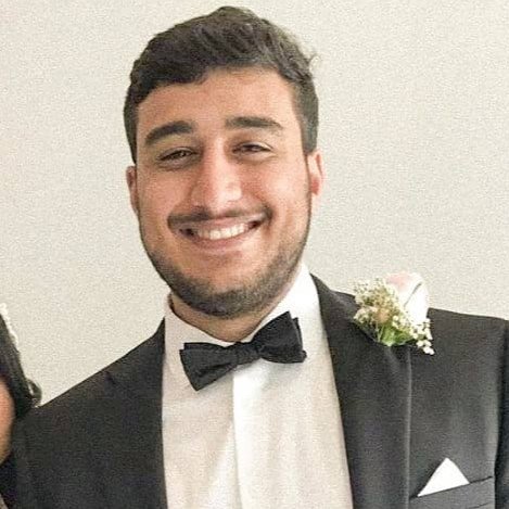 Smiling man in a tuxedo with a bowtie and boutonniere at a formal event.
