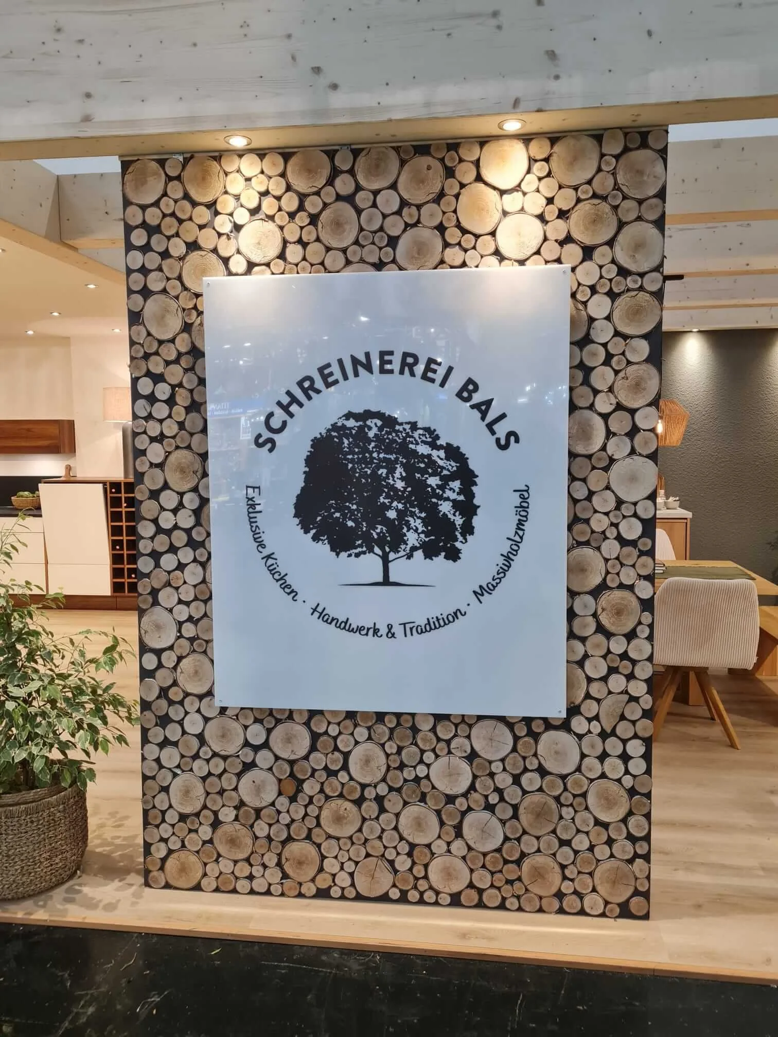  Logo der Schreinerei Bals auf Holzscheiben-Wand am Messestand in München. 