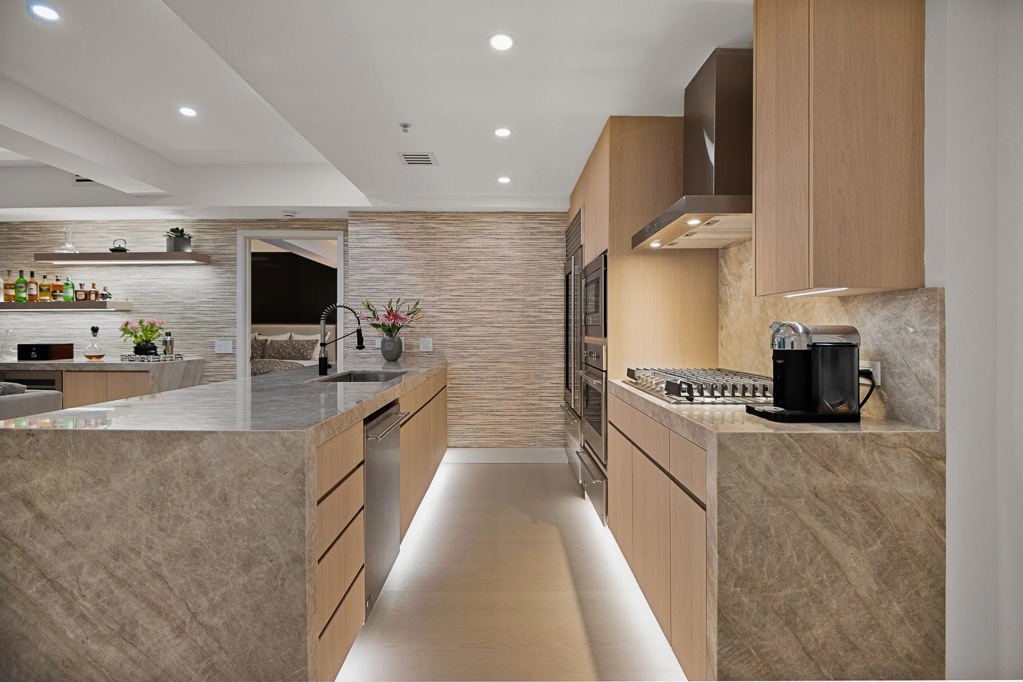 Modern minimalist kitchen with white cabinetry, a marble island, and integrated appliances. Natural light enters through large windows and a skylight. The room features light wood accents and a wooden dining table in Scottsdale.