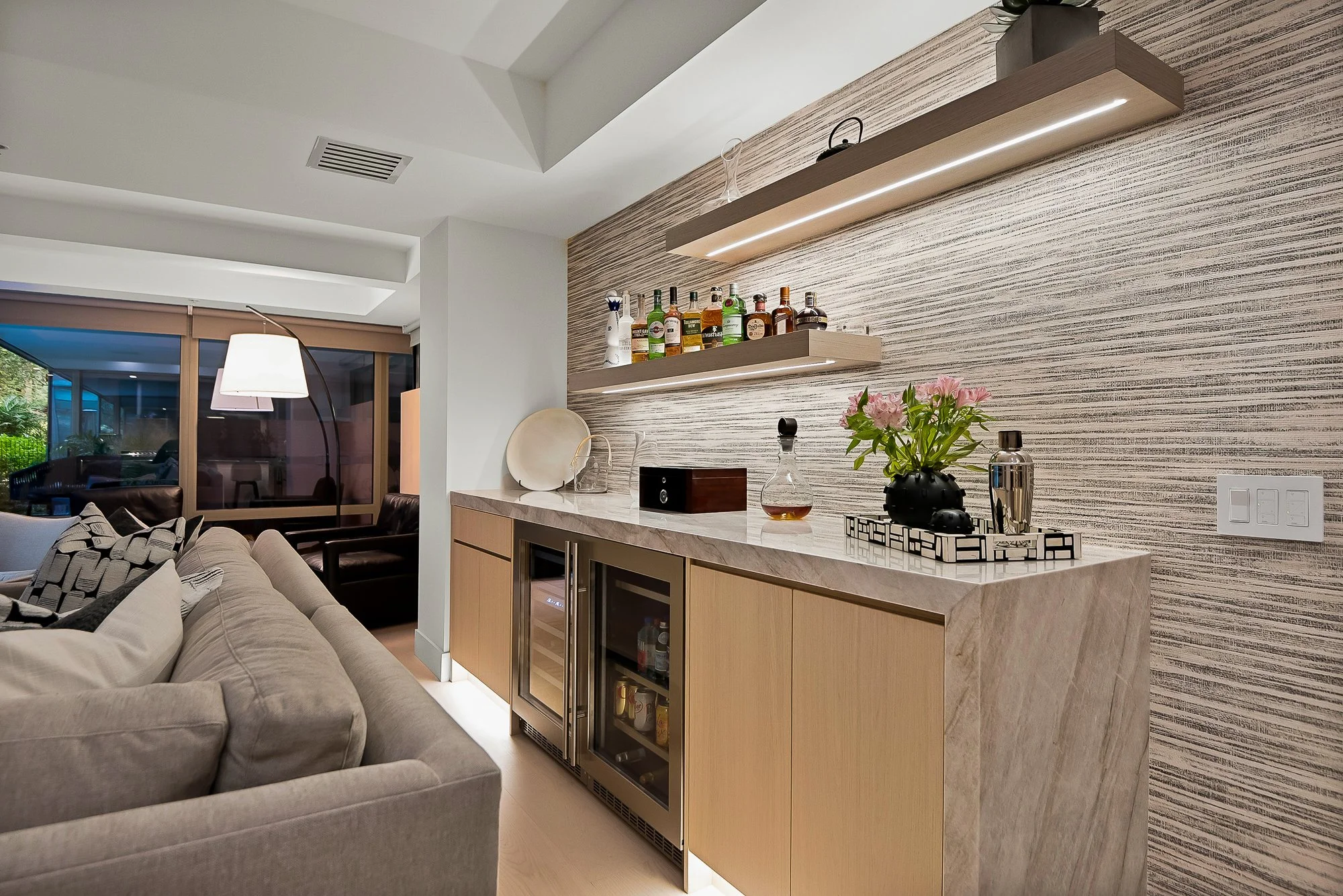 White oak dry bar with integrated wine fridge and beverage cooler, featuring glass upper cabinets and warm under-cabinet lighting