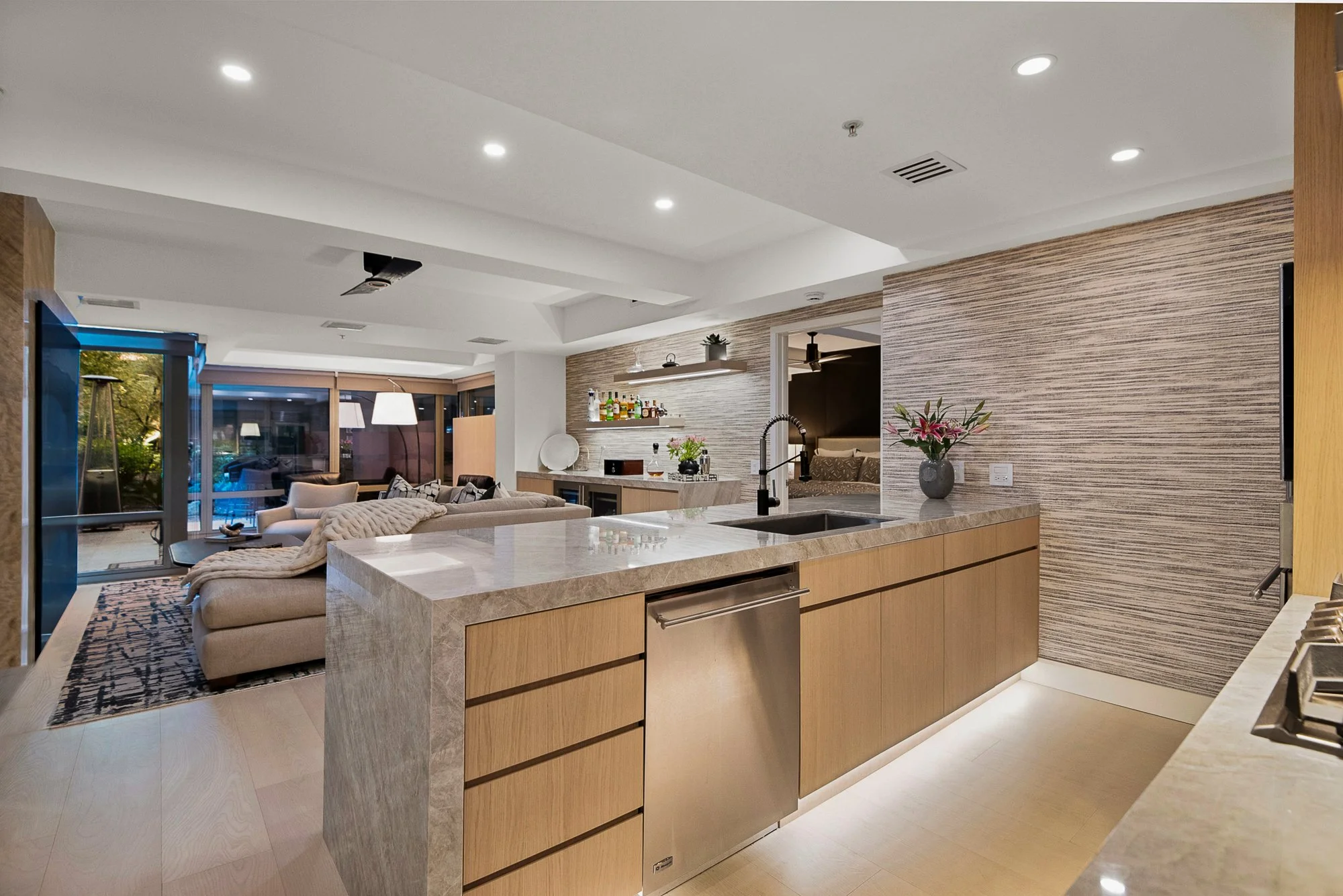Modern kitchen with minimalistic design, featuring a marble island, light wood cabinetry, built-in ovens, and large windows.