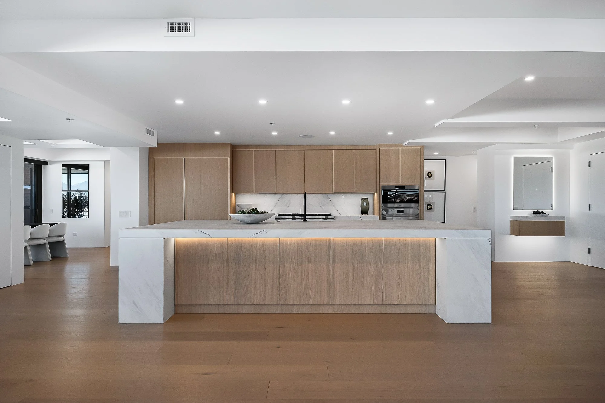 Minimalist dining area with a light wooden table, white chairs, and a round paper pendant lamp in a neutral-toned room.