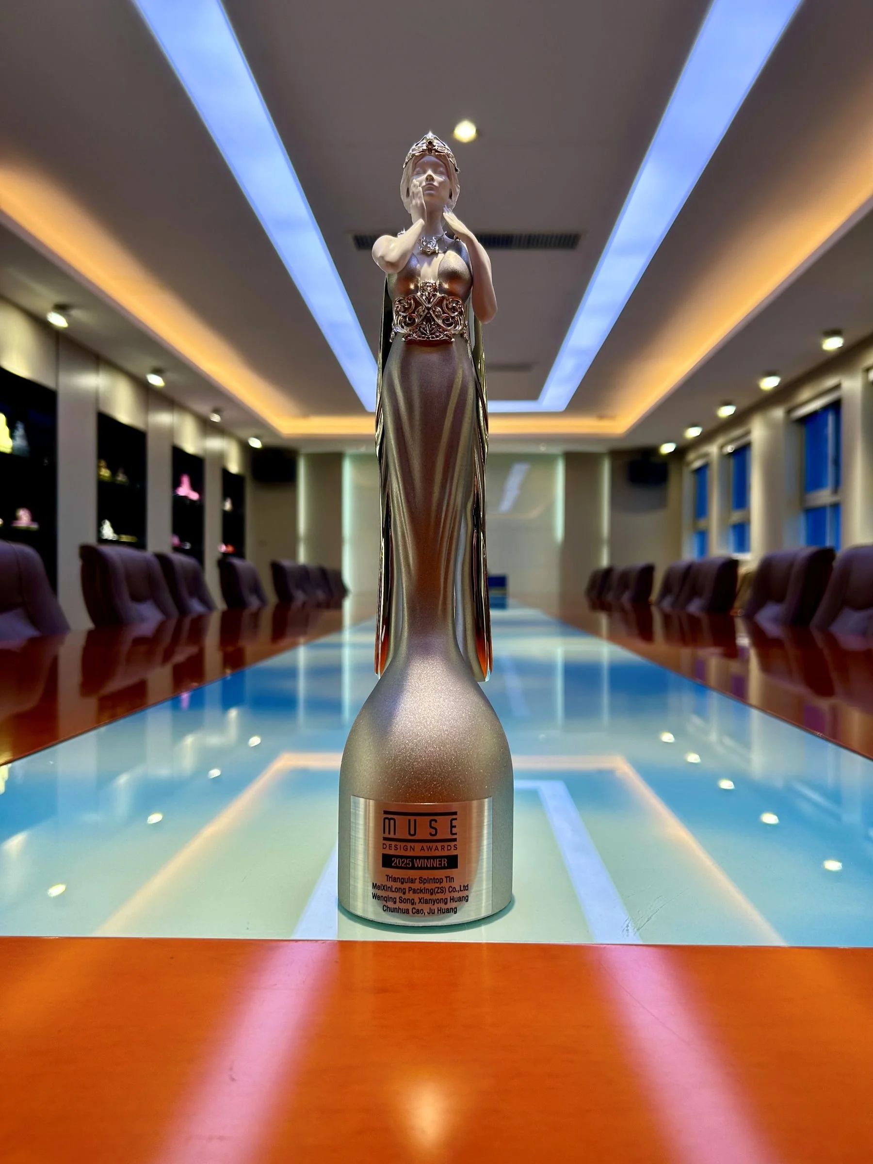 A silver statue of a woman with a serene face, wearing a flowing, glittery gown and a crown-like headpiece, resting on a spherical base.