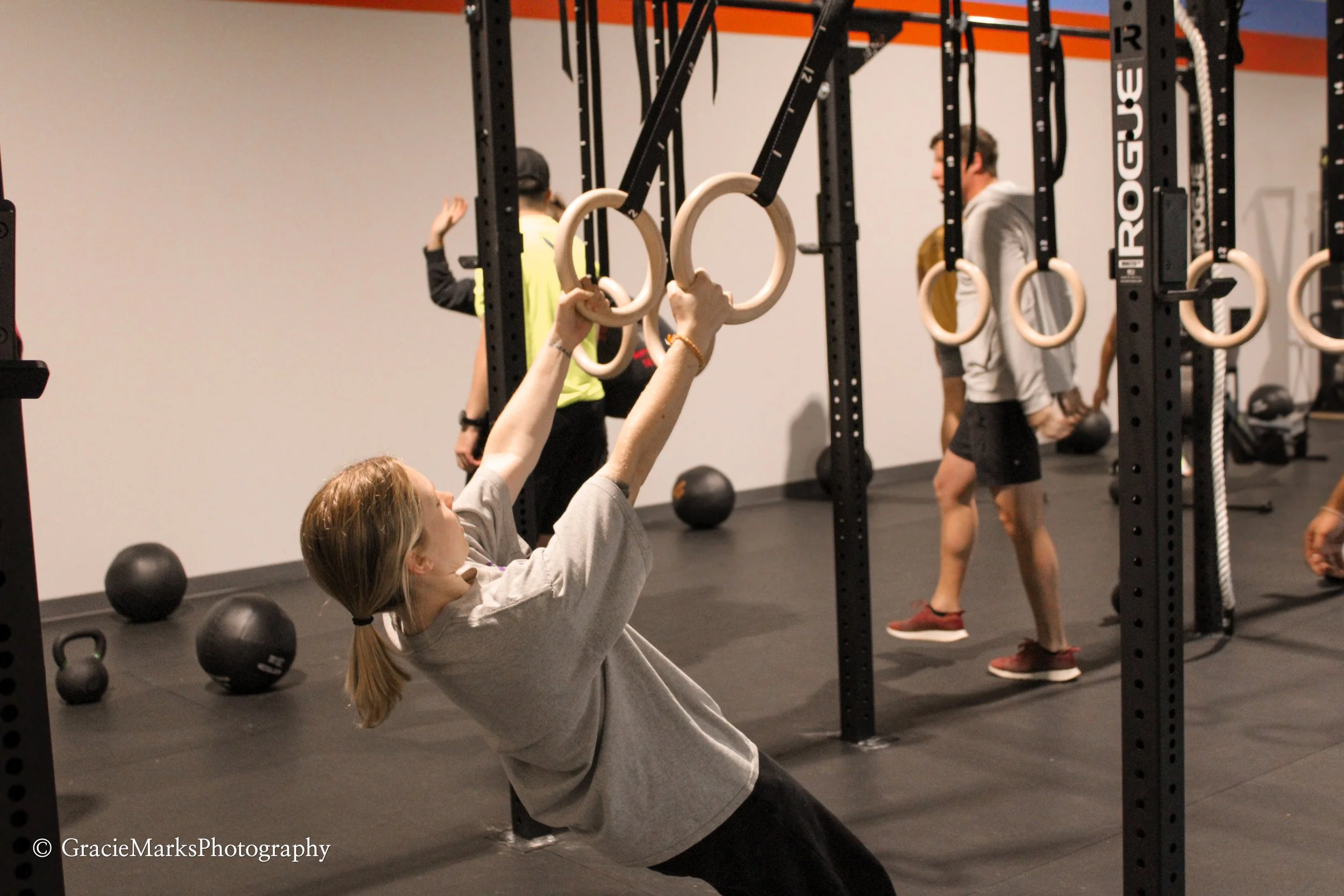 People exercising in a gym, using gymnastic rings for strength training.