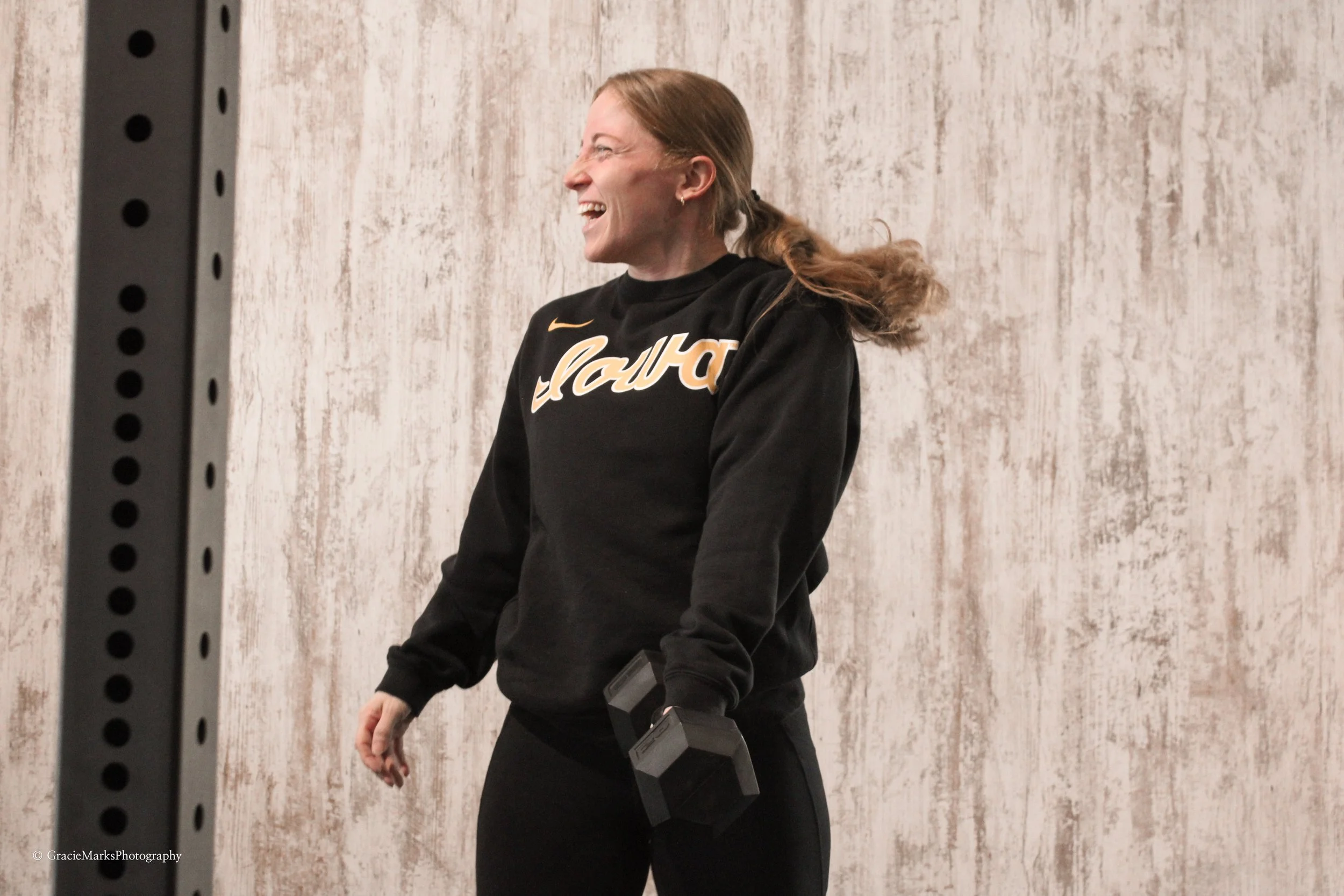 Woman smiling while holding a dumbbell in a room with textured walls.
