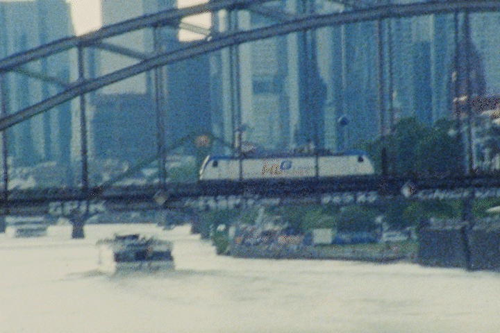 A city scene with a train passing through a bridge over a river or canal.
