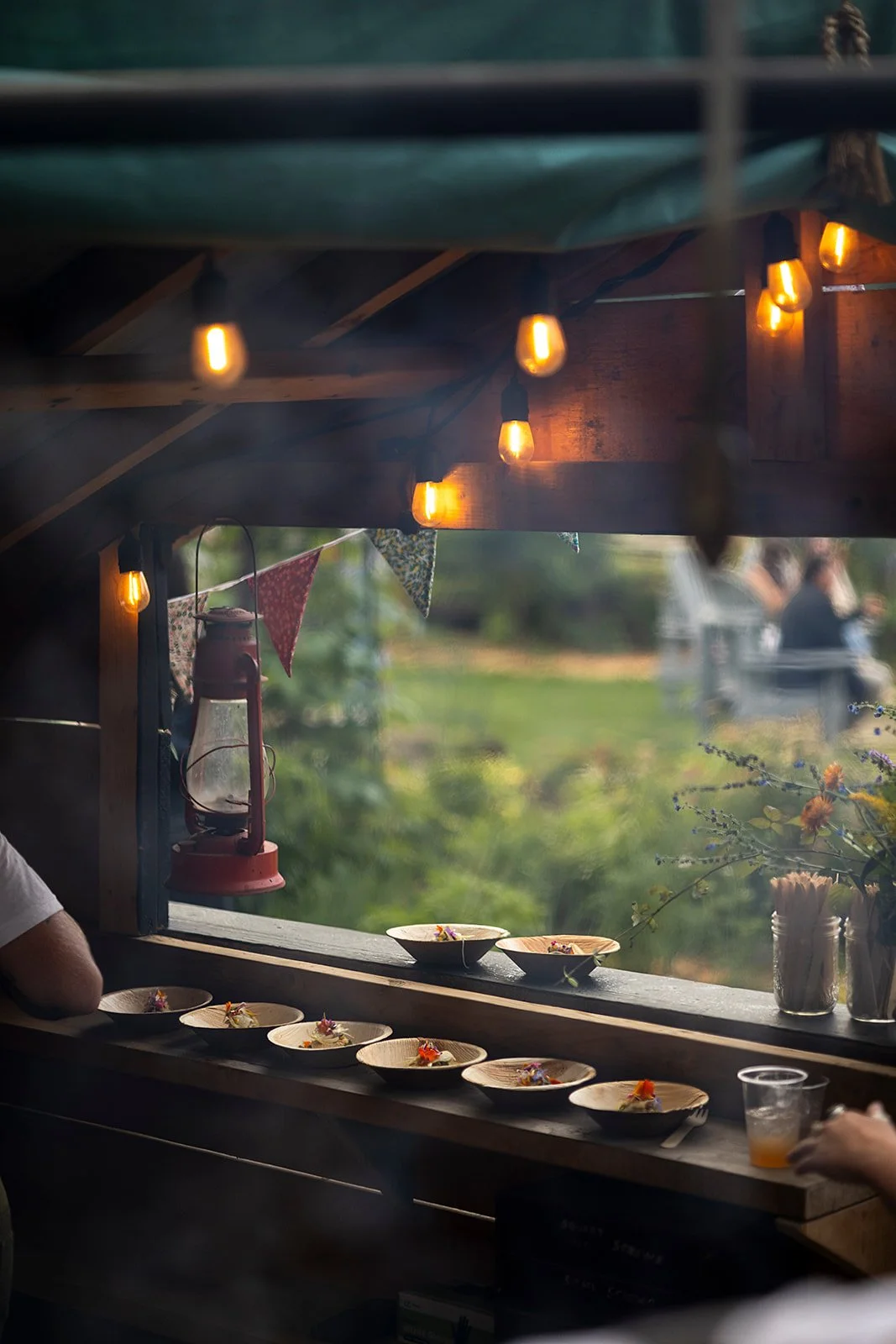 Dishes with food on a wooden counter in an outdoor setting decorated with string lights and a lantern.