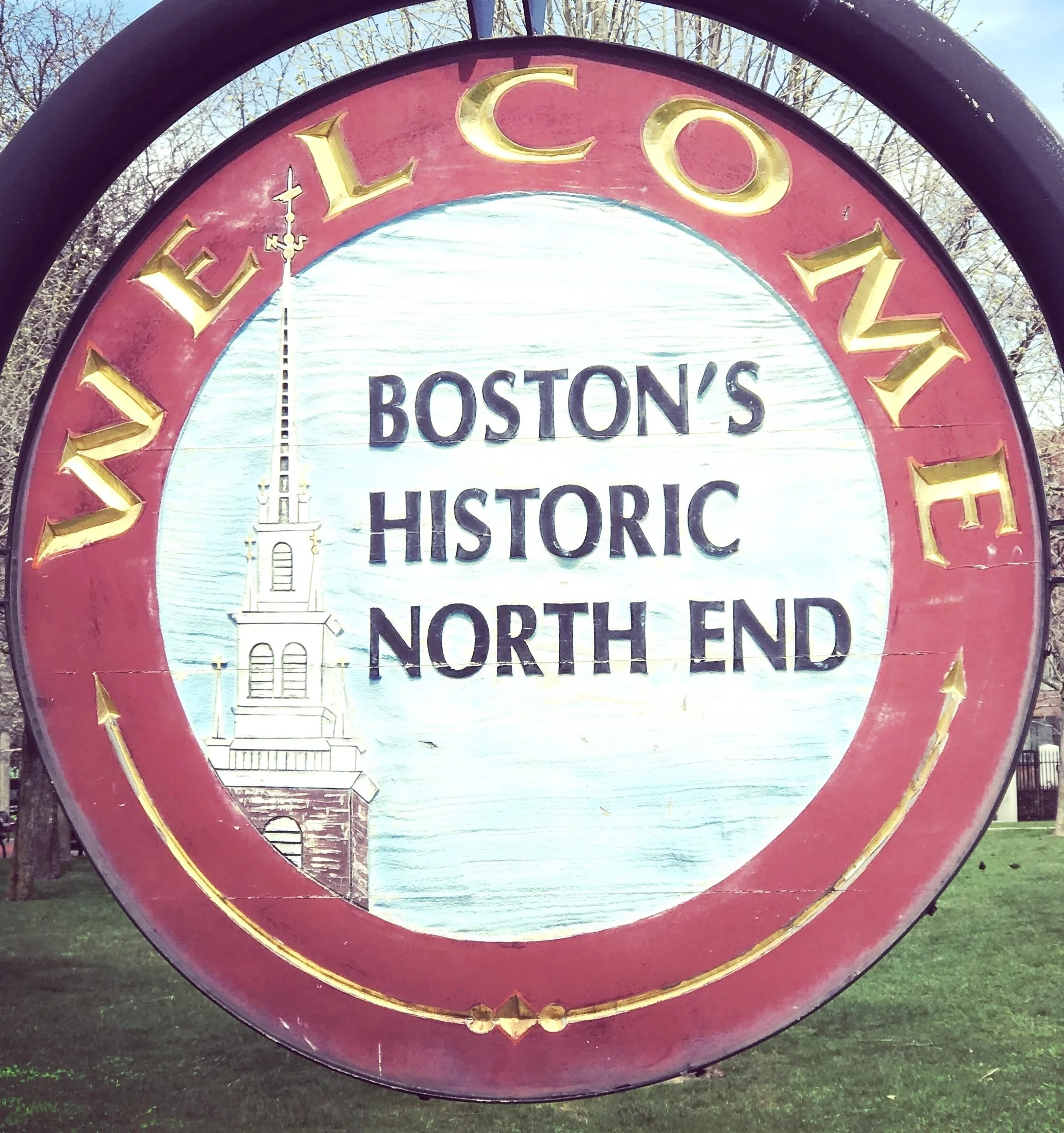 A decorative sign with a red circular border displaying the words 'ELECT' at the top and 'HISTORIC' at the bottom. The inner part of the sign features a painted image of a church steeple with a weather vane on top, set against a light blue sky and some trees in the background.