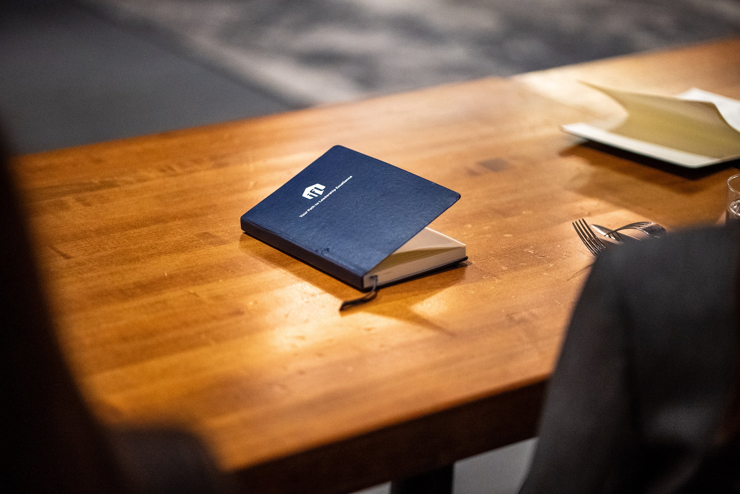 A navy blue notebook with the logo 'FTA' on the cover, resting on a polished wooden table.