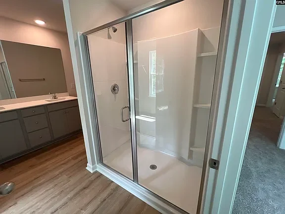 Glass shower enclosure in a bathroom next to a vanity with gray cabinets.