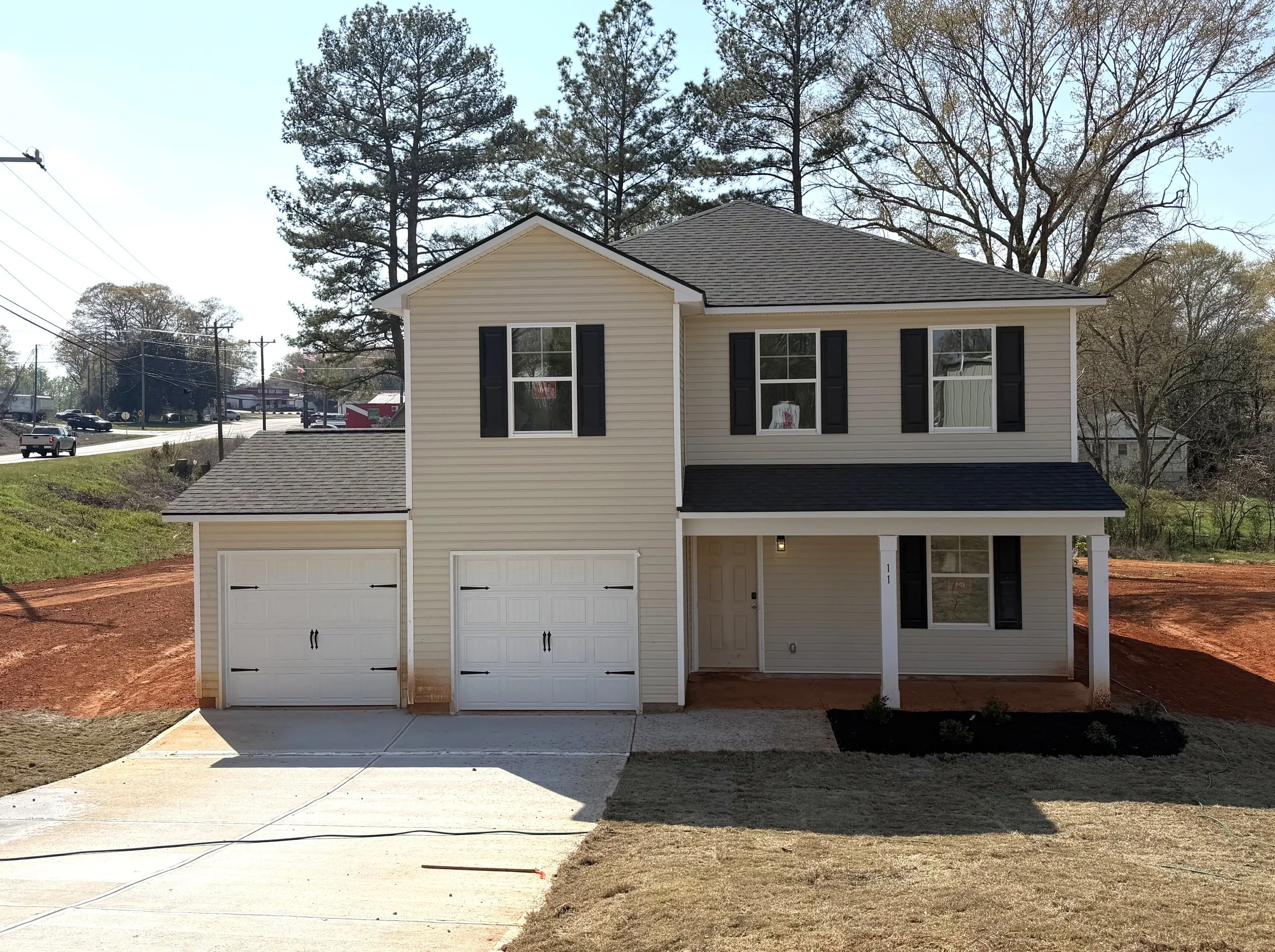 A two-story house under construction, with a black shingle roof and white sheathing with blue logo patterns, snow on the yard, and construction materials inside and outside.