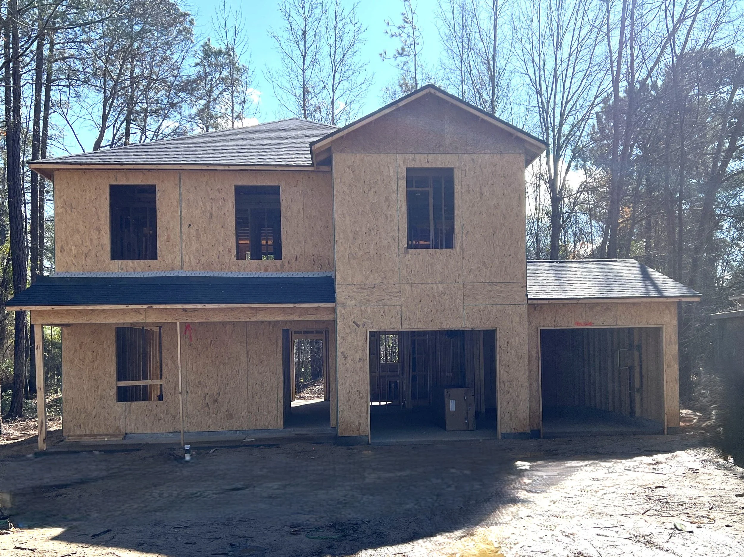 Concrete foundation slab at a construction site with surrounding trees and nearby houses.