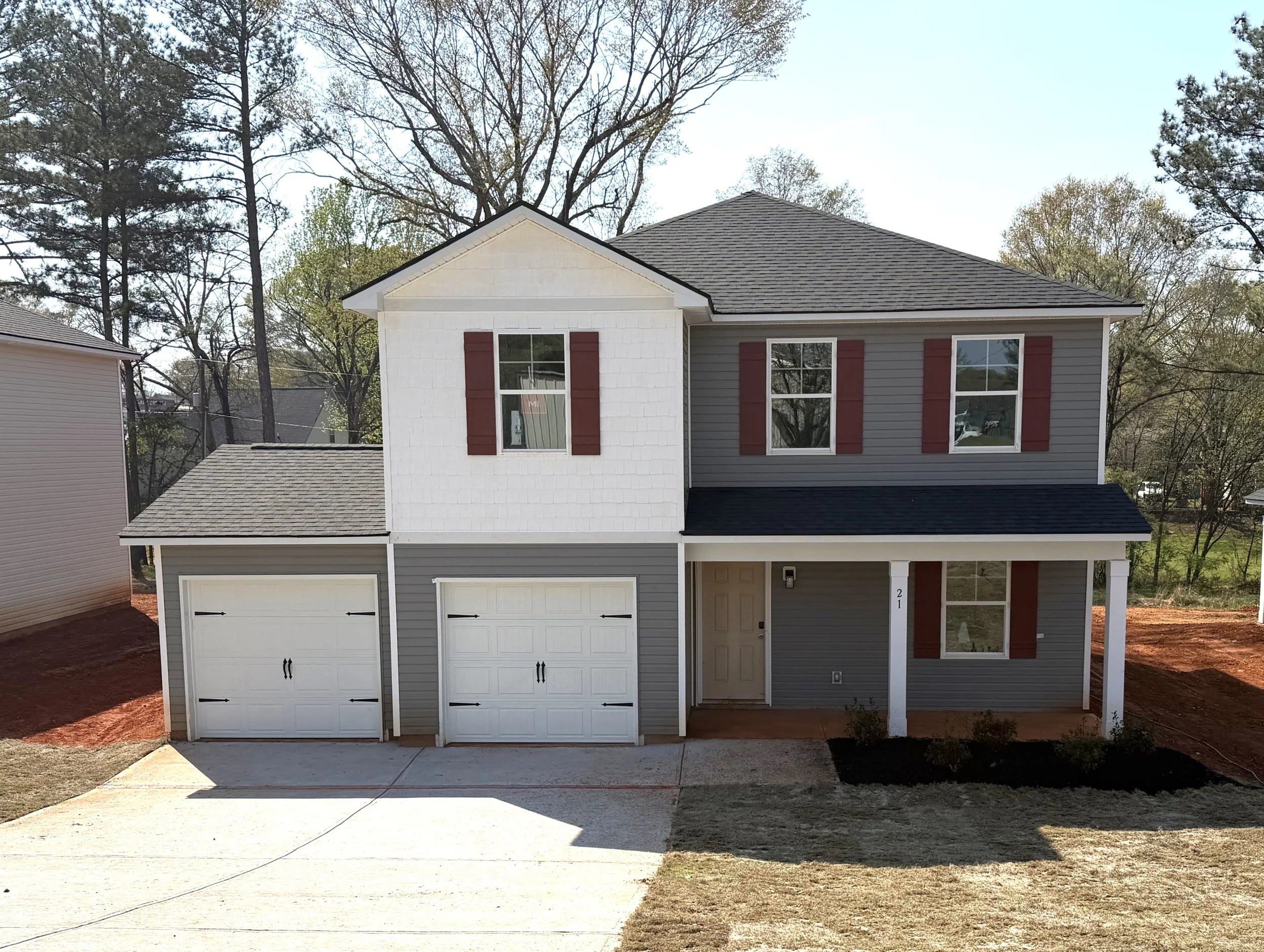 A two-story house under construction with white building wrap, two attached garage spaces, and snow on the ground.