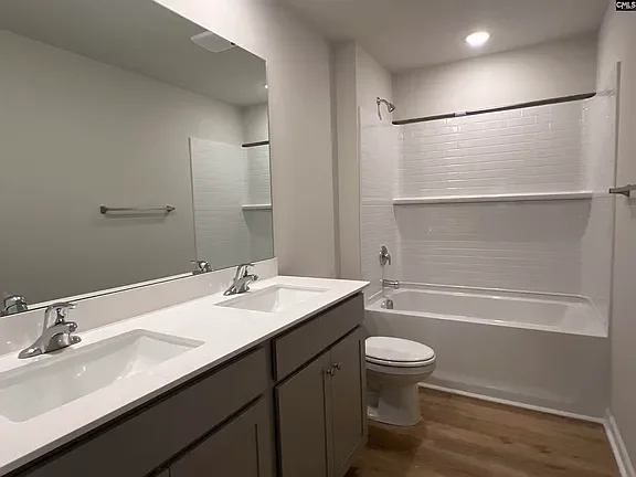 Bathroom with dual sinks, a large mirror, a toilet, and a bathtub with a sliding curtain rod, white tiled wall, and wooden flooring.