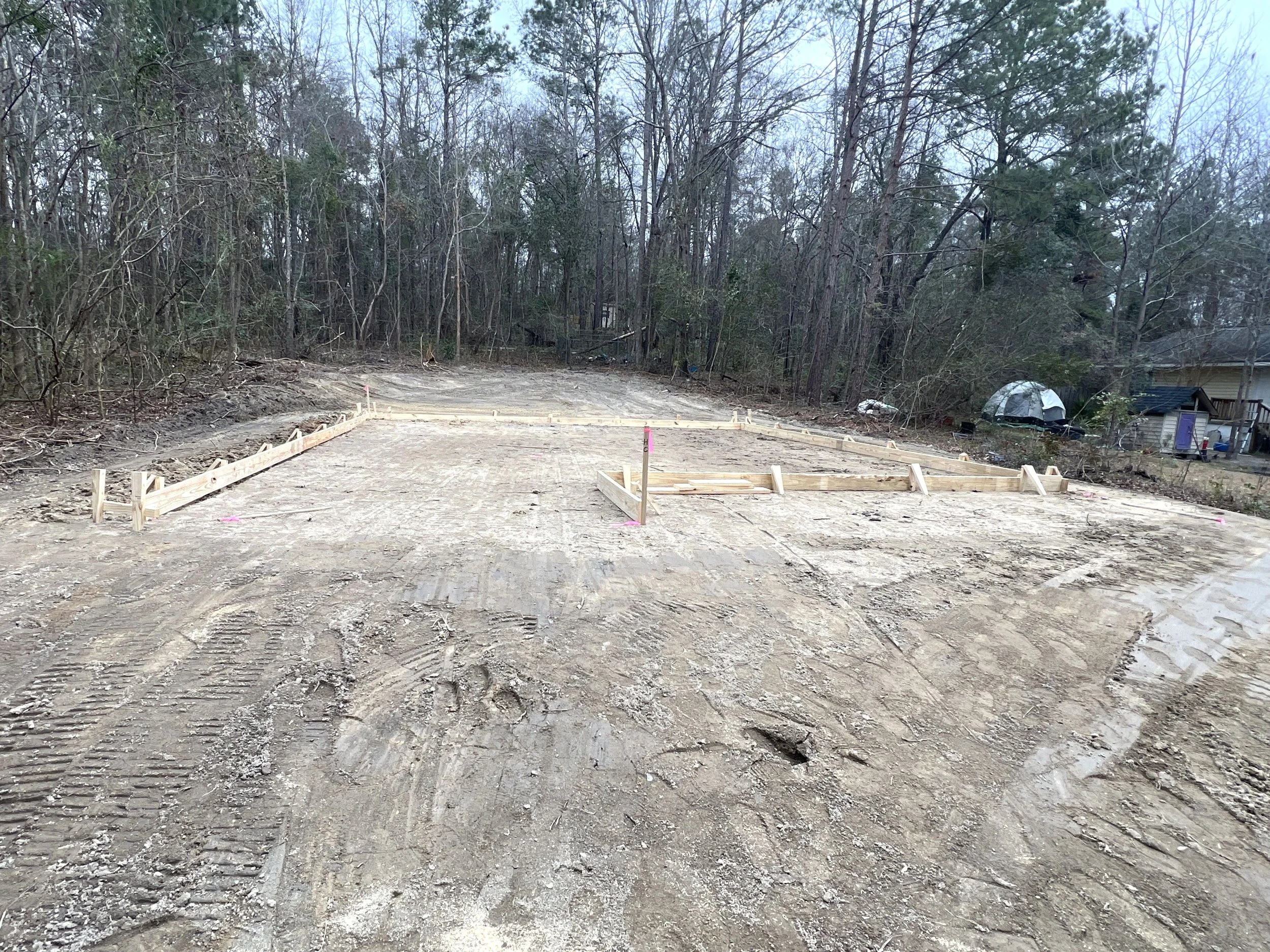 Concrete foundation slab at a construction site with surrounding trees and nearby houses.