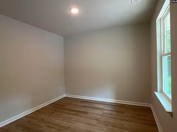 Empty room with beige walls, hardwood floor, a window, and a ceiling light.
