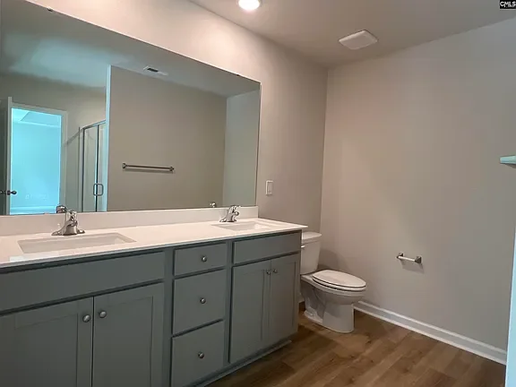 Bathroom with double sink vanity, large mirror, toilet, and wood flooring.
