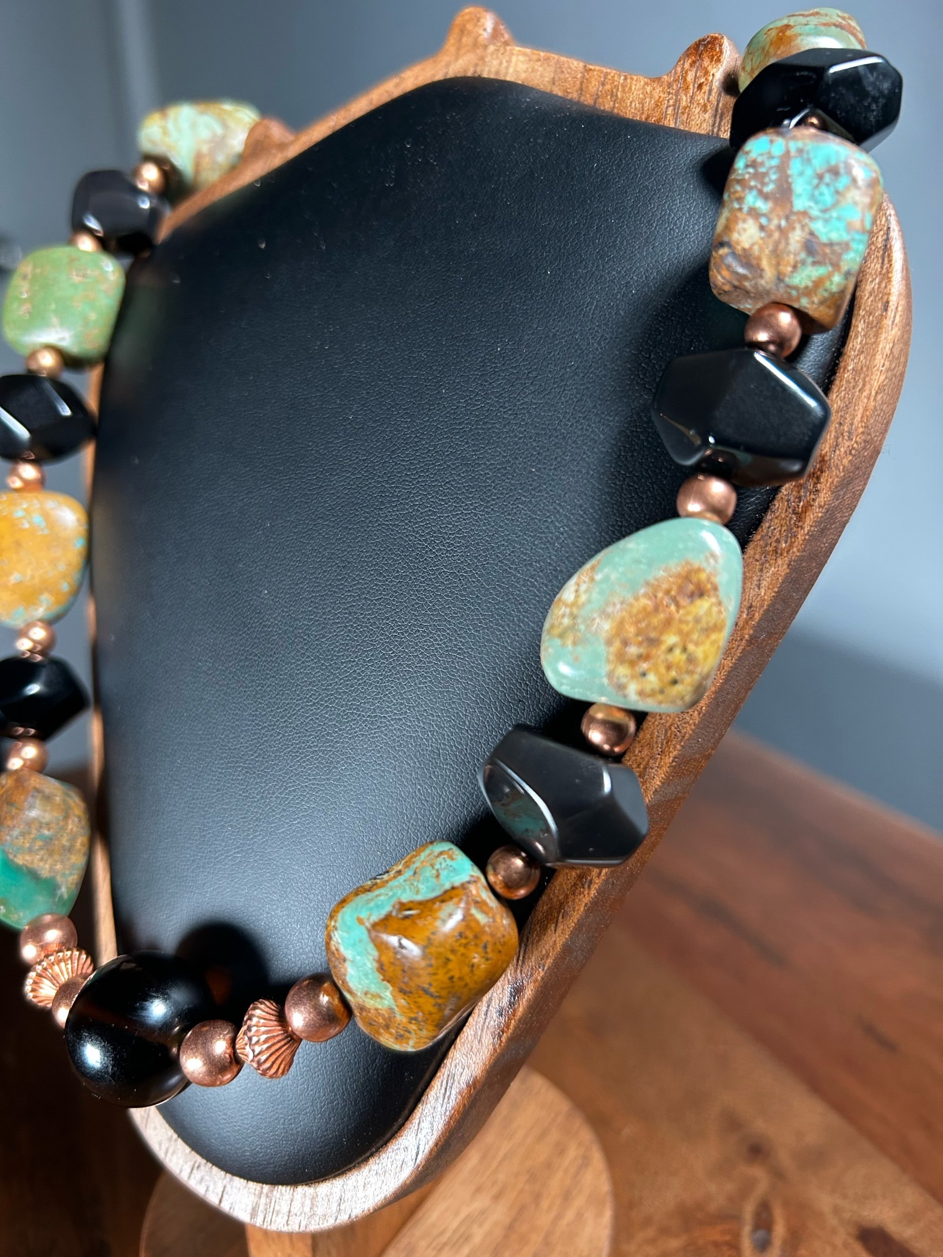Close-up of a beaded necklace with large stones and beads, resting on a black display stand with a wooden edge.