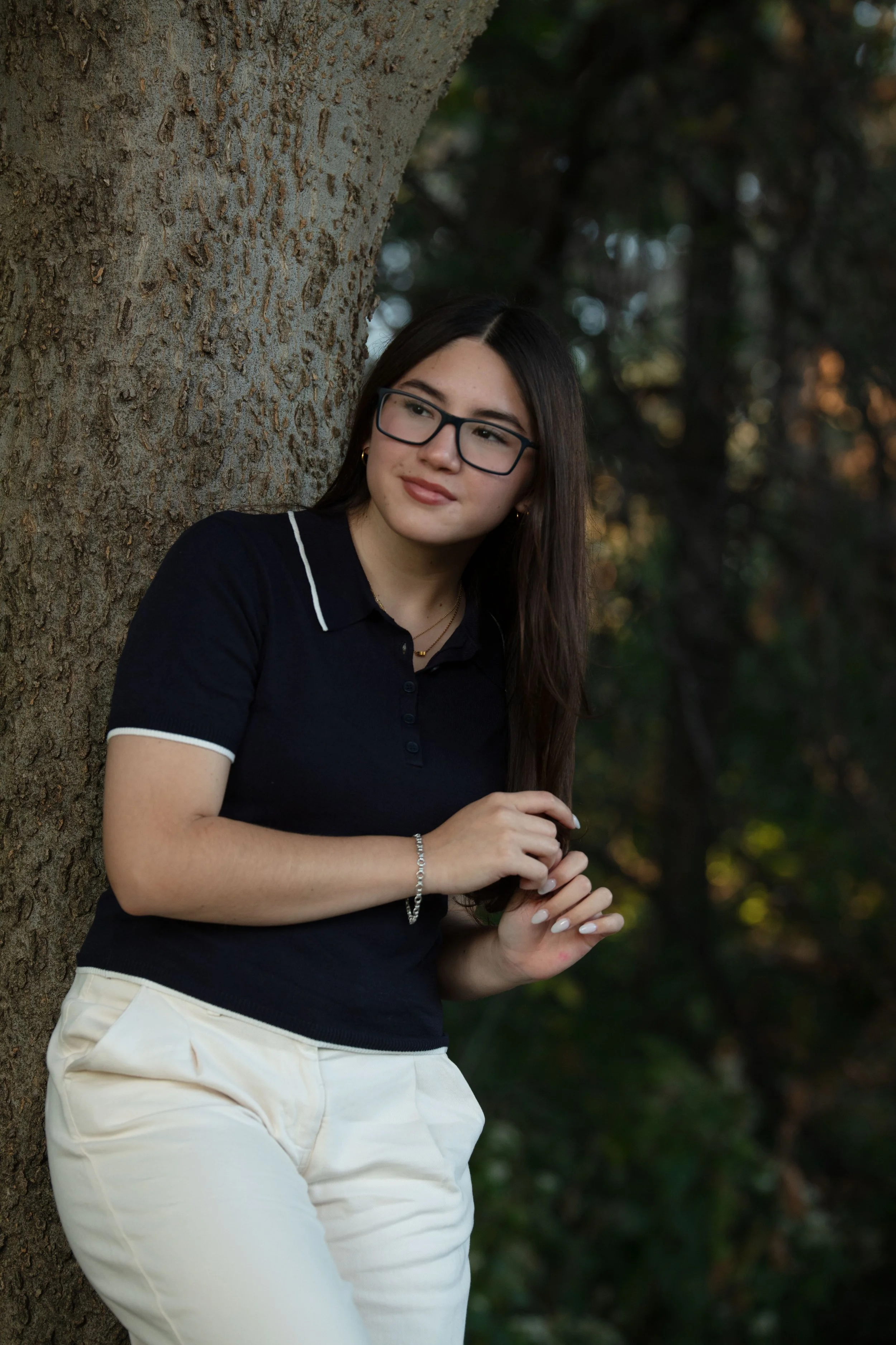 Senior leaning up against the tree playing with her hair