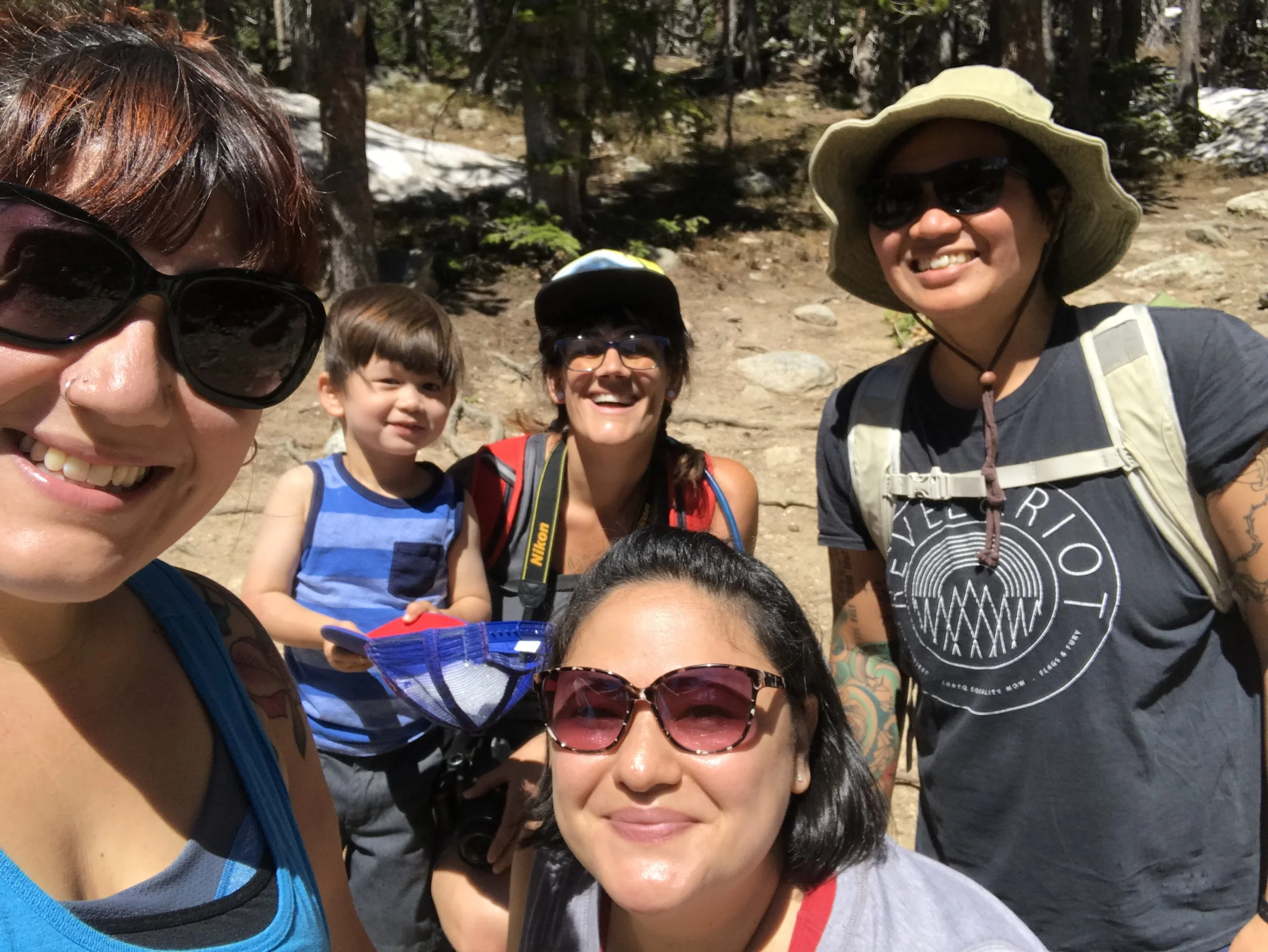 Group of people smiling outdoors on a sunny day, with trees in the background.