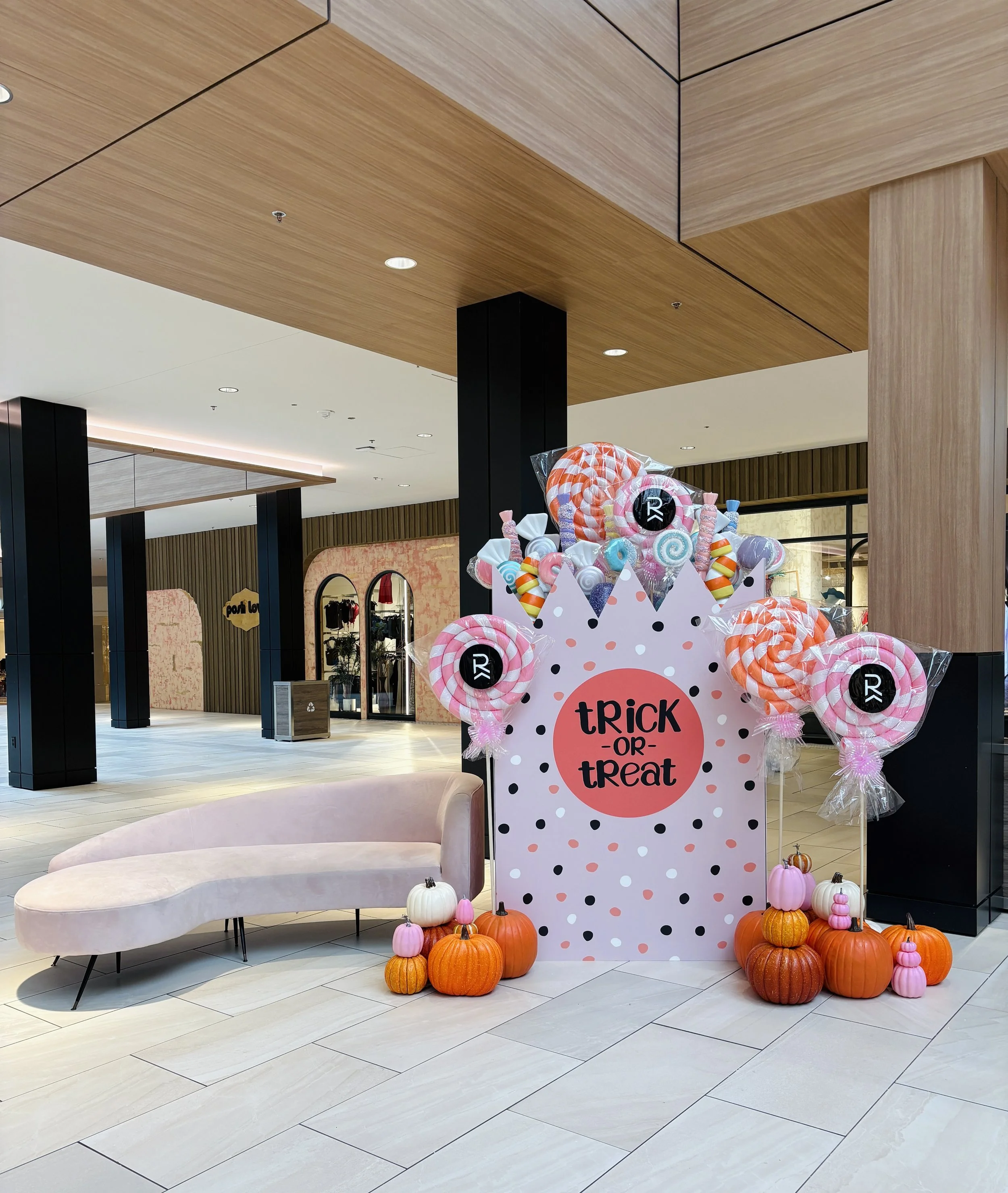 Commercial Halloween seasonal styling at Rosedale Center featuring a pastel trick-or-treat photo display with giant lollipops, pumpkins, and a pink velvet couch.