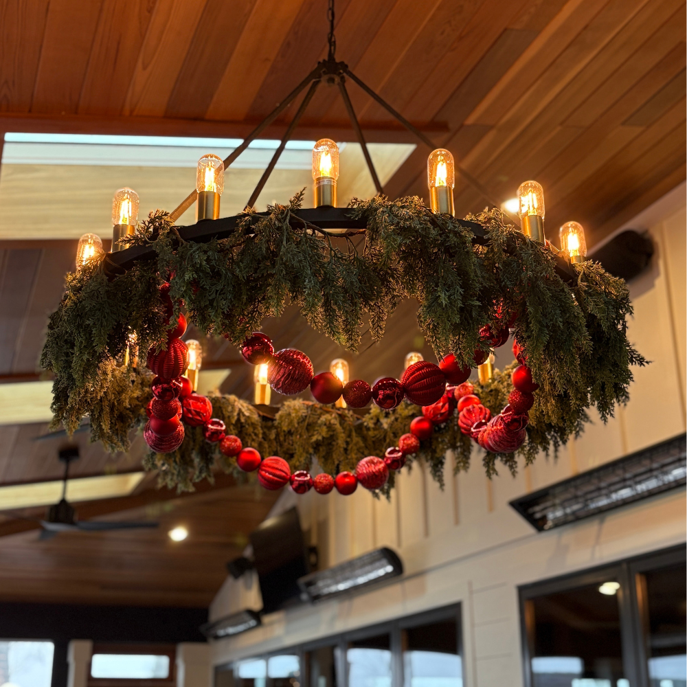 Commercial seasonal styling at Maynard's Excelsior featuring a large circular chandelier decorated with evergreen garland and red ornaments.