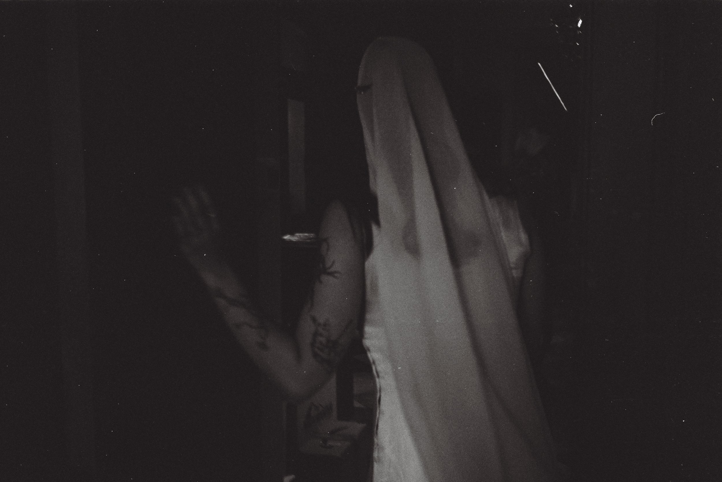 A person with long hair wearing a sleeveless top, taking a selfie in a dark room, with a tattoo on their arm visible.