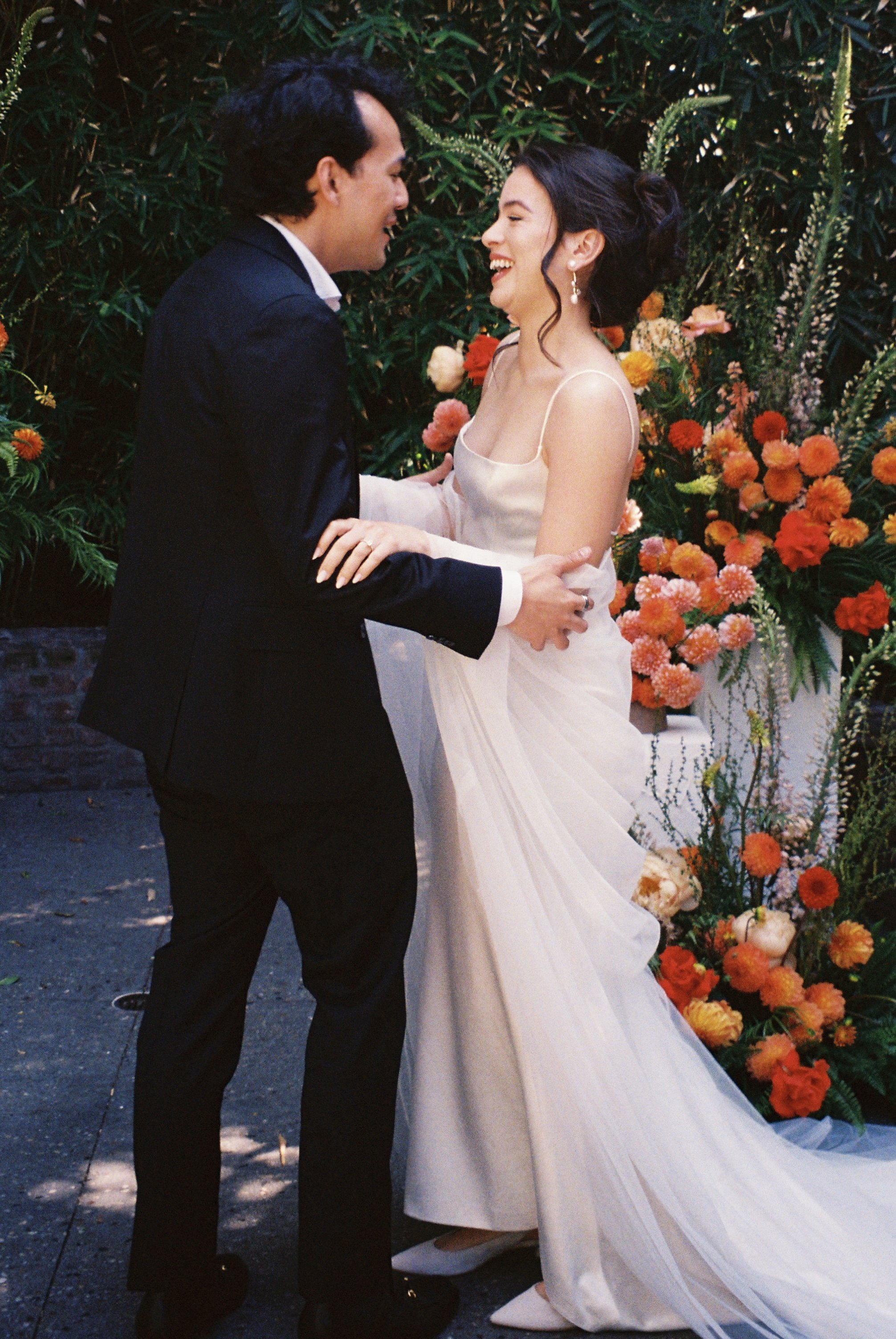 A bride and groom dancing at their wedding, surrounded by orange and pink flowers and greenery.