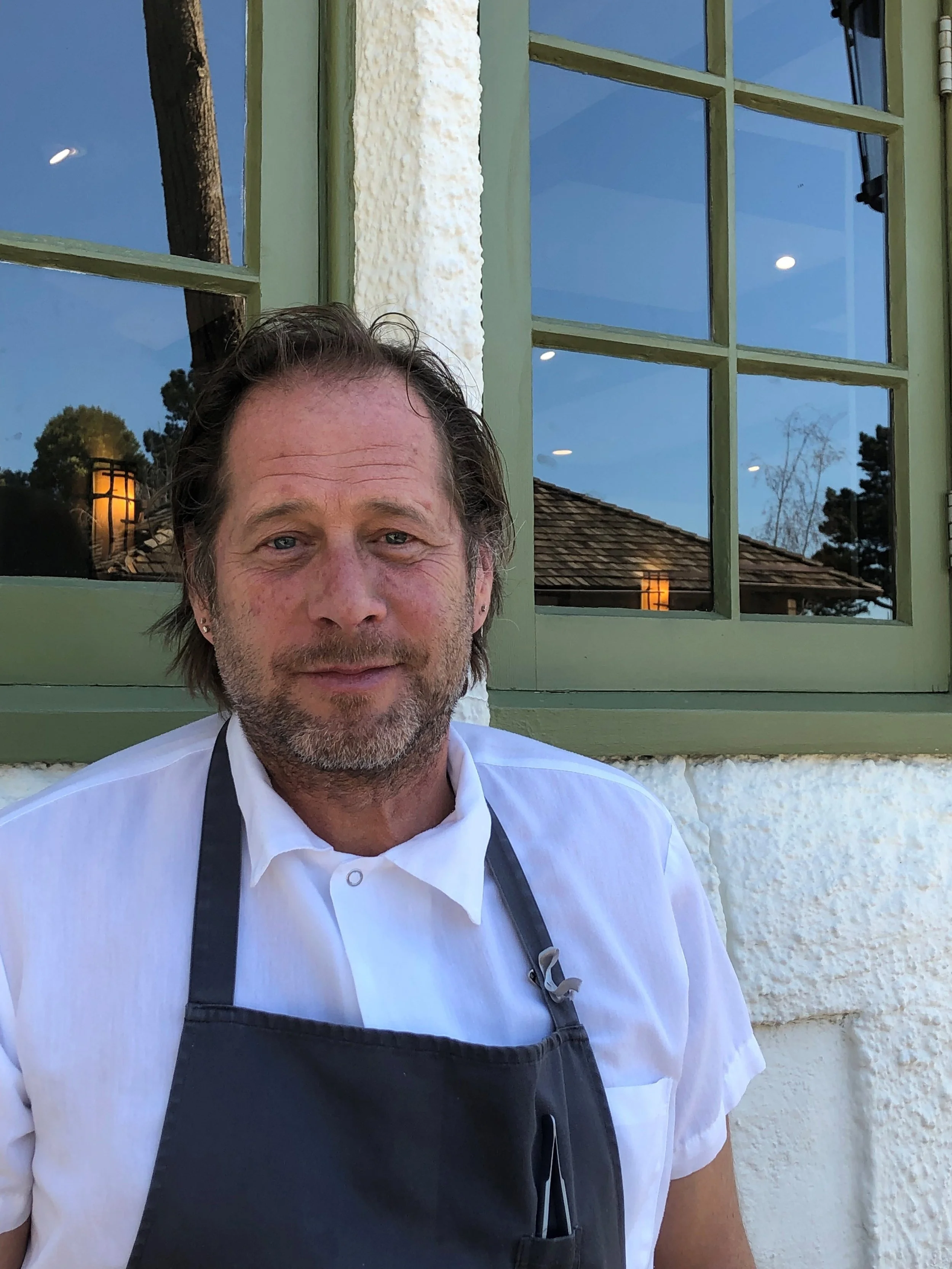 Headshot of David Kinch wearing a white Chef's coat and gray apron.
