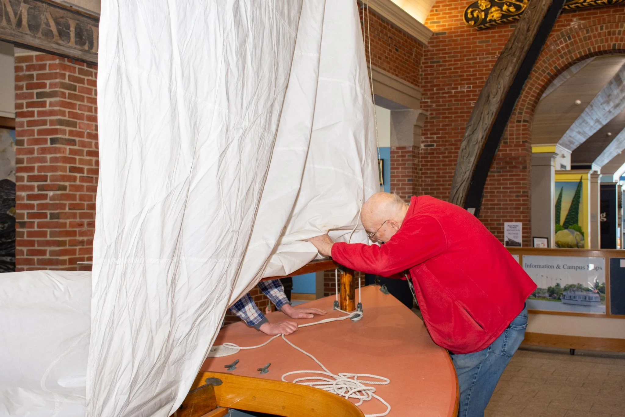 Two people are working on a science experiment involving a large white sheet and a wooden structure inside a building with brick walls and decorative elements.