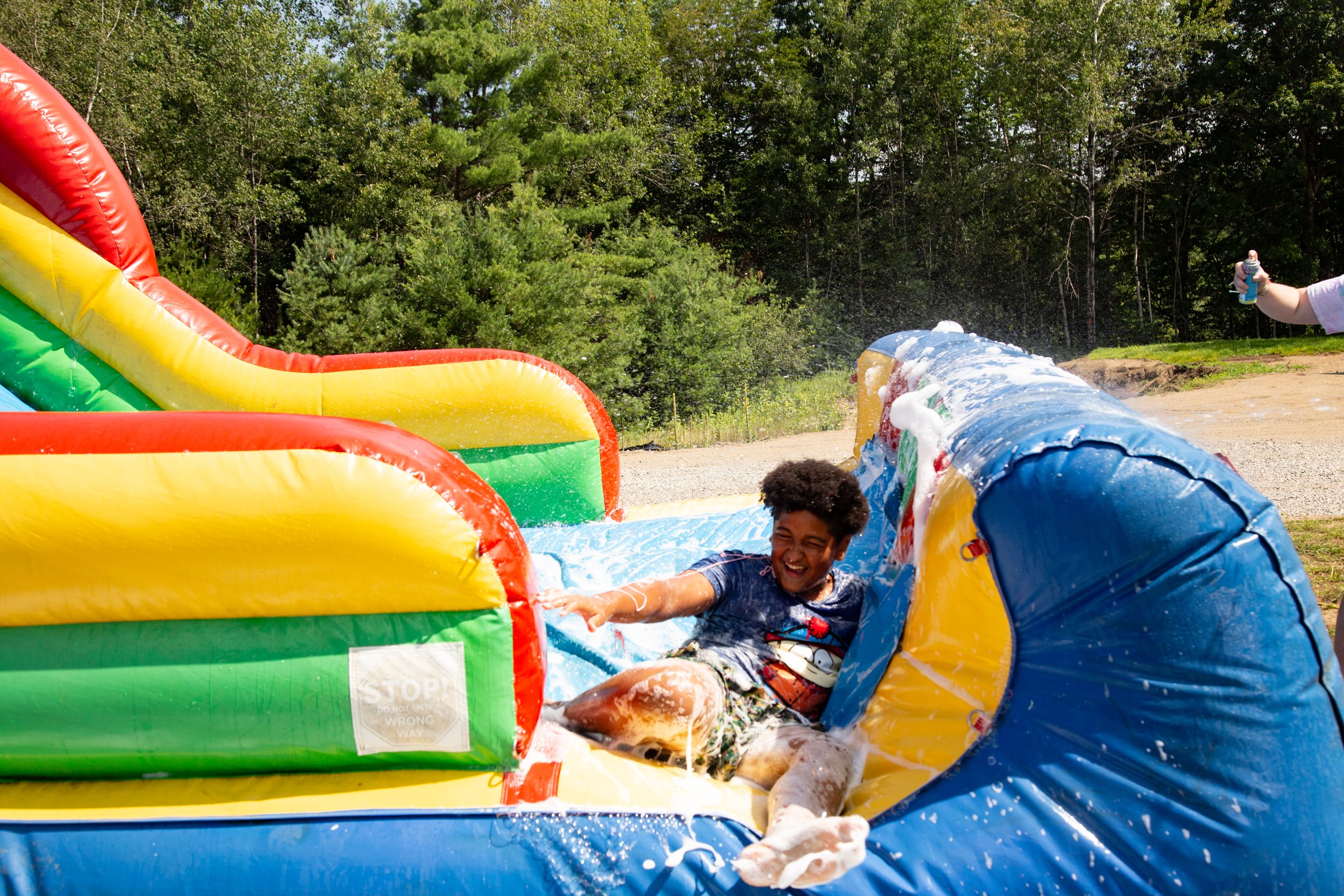 Kid at sleep away camp sliding down water obstacle course.