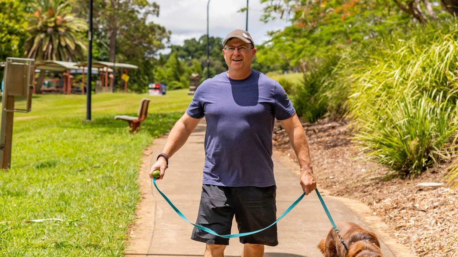 A man walking a dog on a leash in a park on a sunny day.