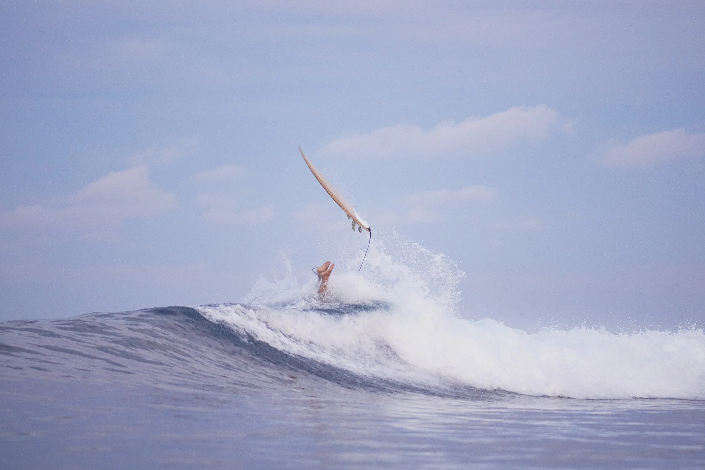 Person falling off surfboard in the ocean waves during daytime.
