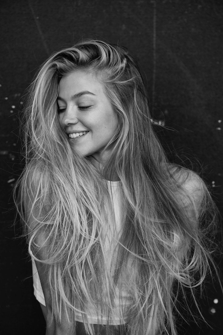 Black and white photo of a young woman with long, tousled hair smiling with closed eyes.