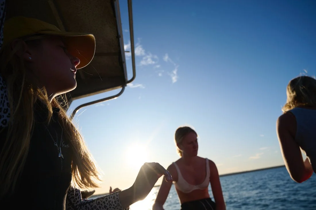 Three women on a boat during sunset, with the ocean in the background.