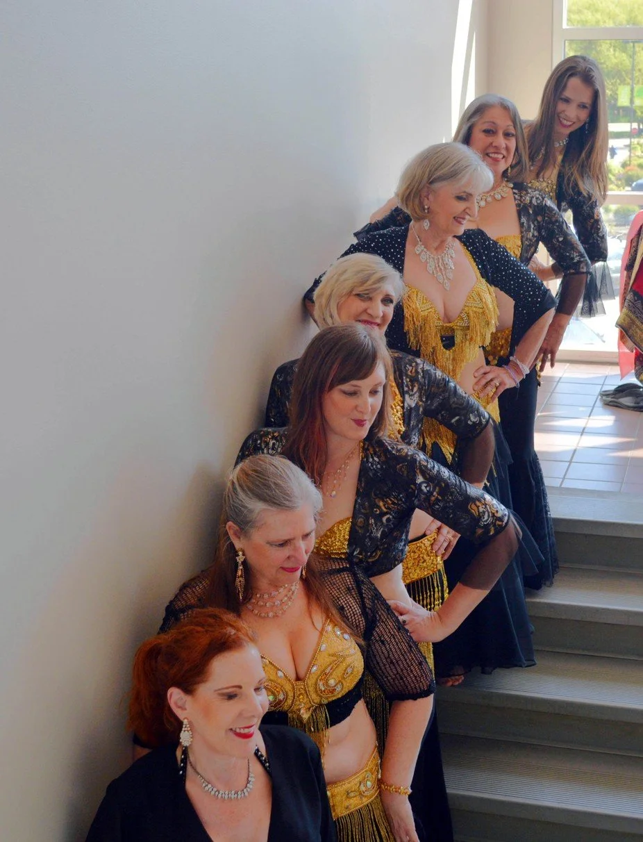 Lara Victoria Belly Dance Students all in a line going up stairs. They all smile and pose dressed in elegant black and gold costumes. Lara Victoria Belly Dance Students having fun!!