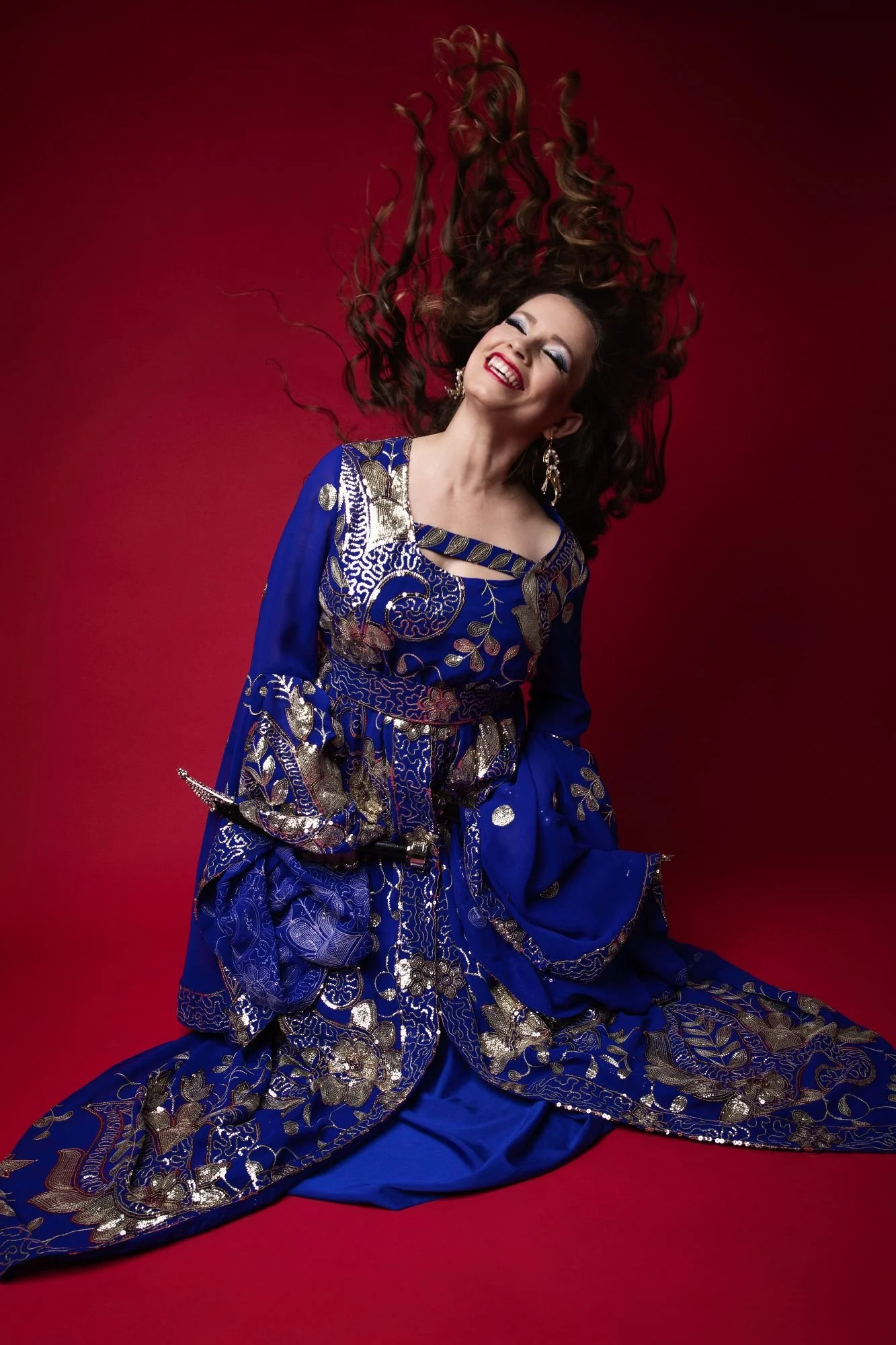 Lara performing Iraqi hacha'a dance. Here hair is tossed into the air. She wears a blue dress with silver sequins. She is dancing with daggers.