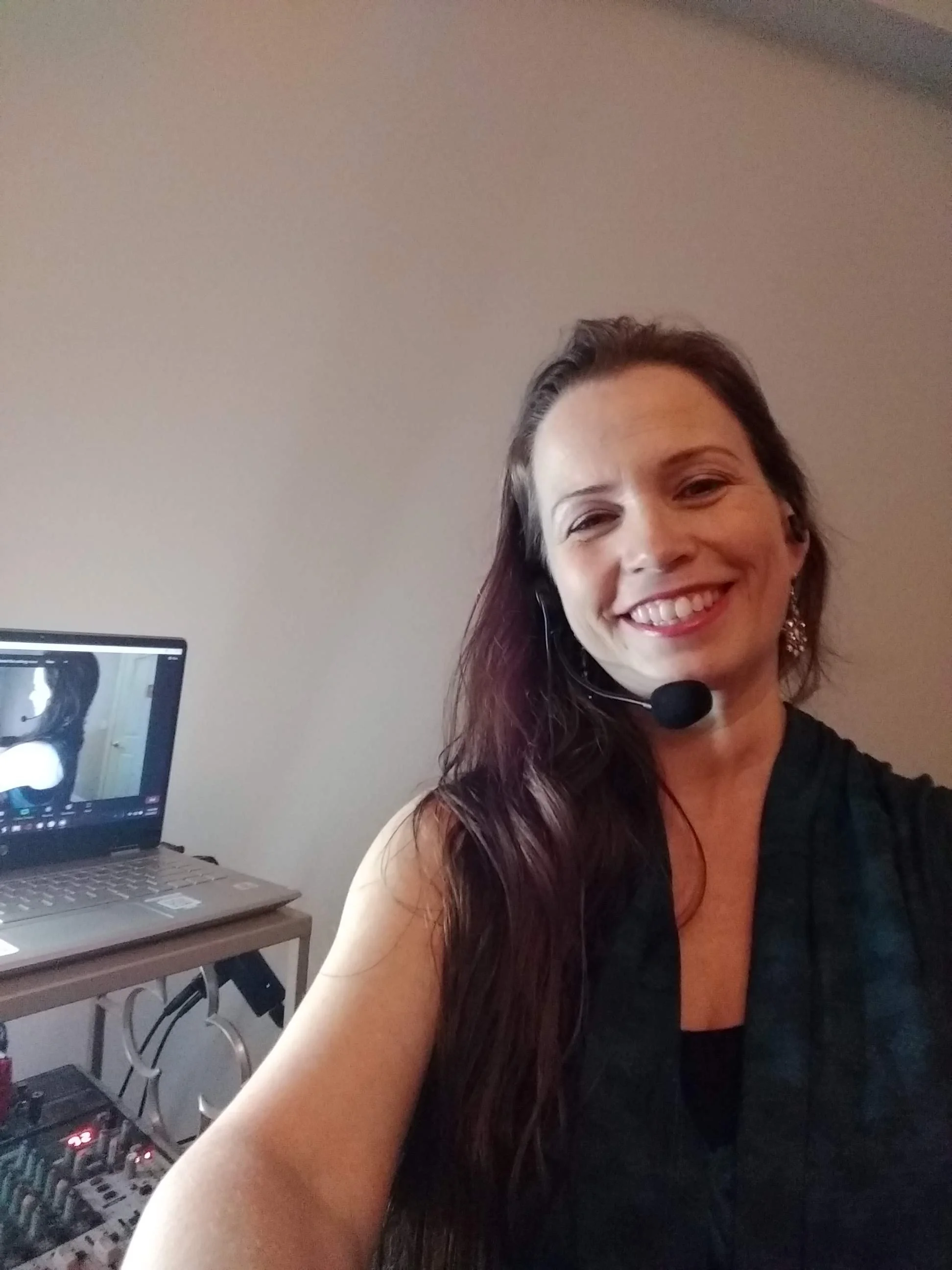 Lara Victoria Olympia Belly Dance Teacher smiles in front of a computer, wearing a microphone to teach online dance classes. Membership is through Patreon. Classes run through Zoom. Learn Belly Dance from Lara from any location in the world, anytime.