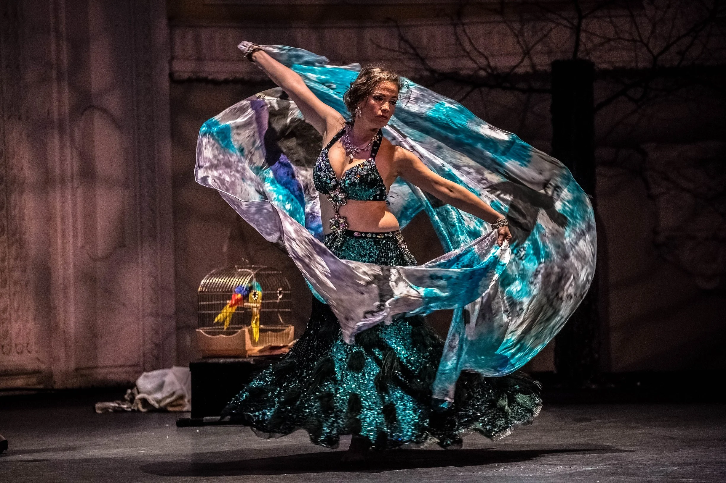 Lara Victoria bellydancer performs for Horrific Bellydance Show at Tacoma Pantages. She is spinning in her green feathered costume amid two half circle veils painted with crows.
