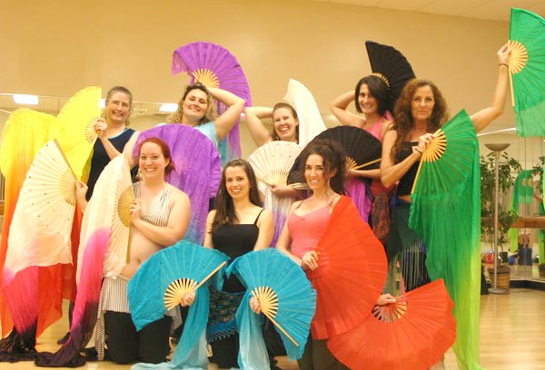 Workshop students posing for end-of-class photo. There are 7 students. Lara is front and center. Everyone is holding their fan veils out in a pose. Some fans are held to the left, some to the right, some overhead, and some low. The fans are colorful.