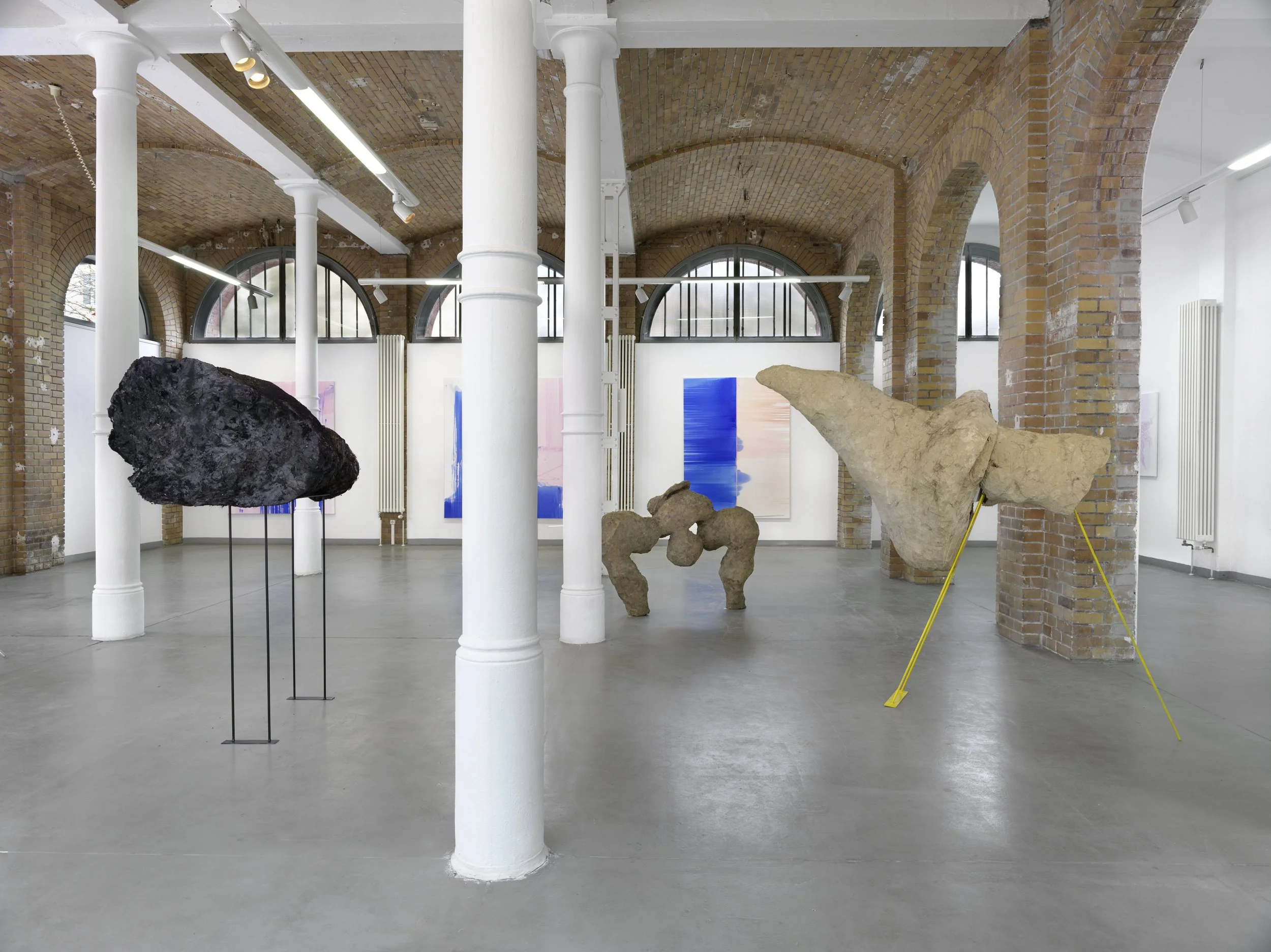 Installation view of Unterm Lederhimmel by Marie Birkedal and Gloria Zein at Alte Feuerwache, 2024, with Gloria Zein’s dark sculpture beneath the brick arches and Marie Birkedal’s paintings visible in the exhibition space.