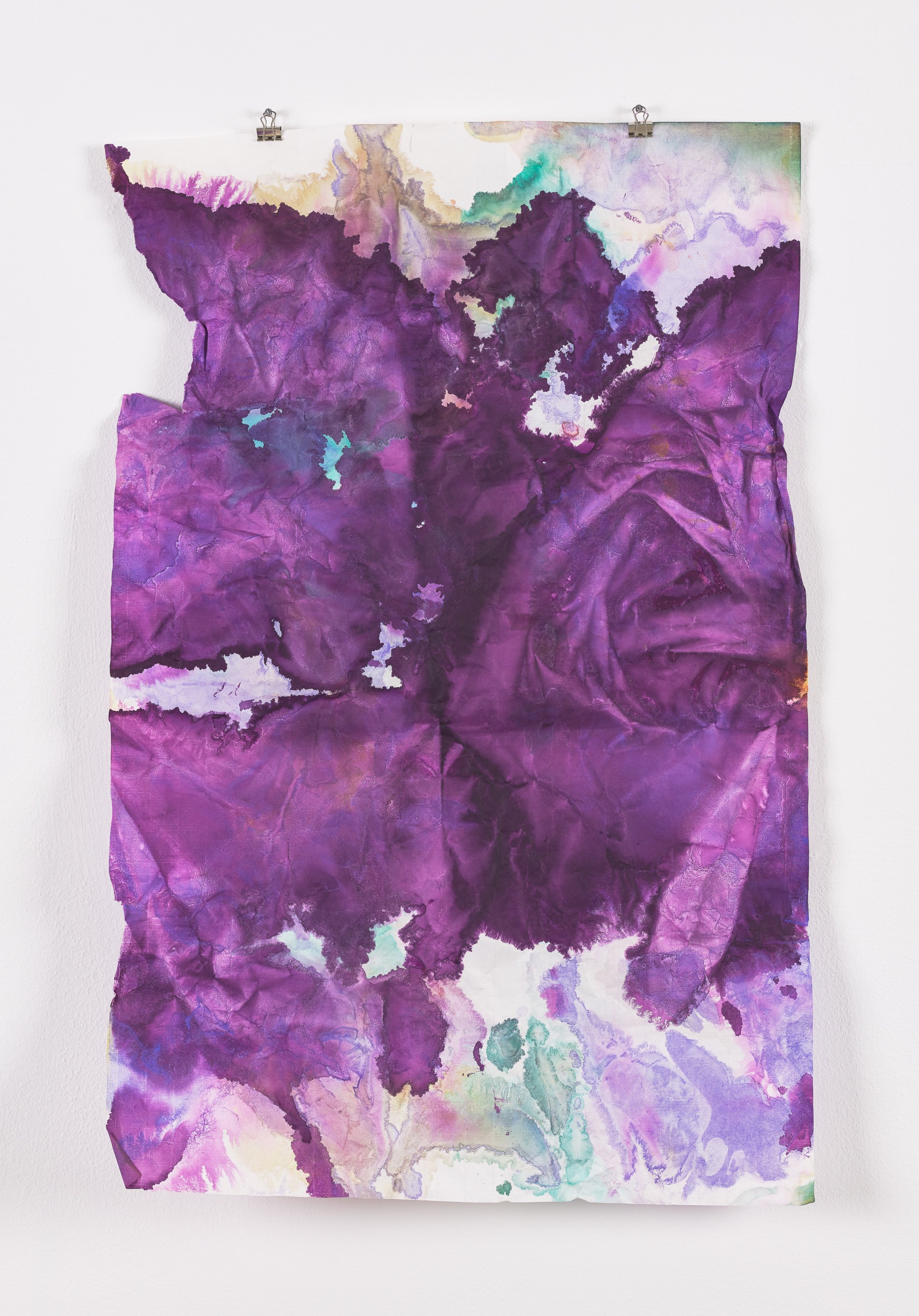 Abstract watercolor painting with shades of purple, pink, green, and beige, hanging on a white wall with metal clips.