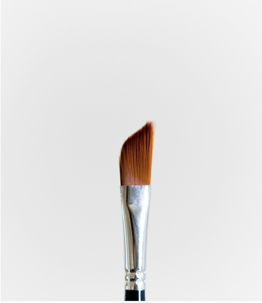 A minimalist close-up of an angled paintbrush, photographed against a soft white backdrop.