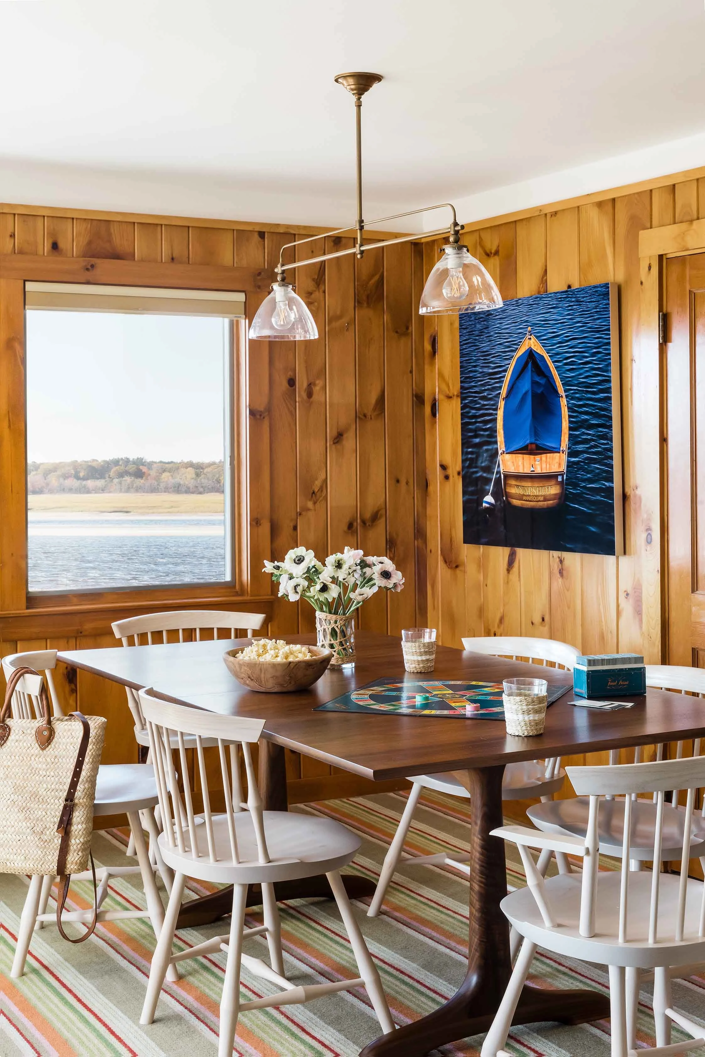 Wooden dining table with white chairs and interior wooden siding at the Cozy Seaside Cottage in Wells, ME - Kate Maloney Interior Design
