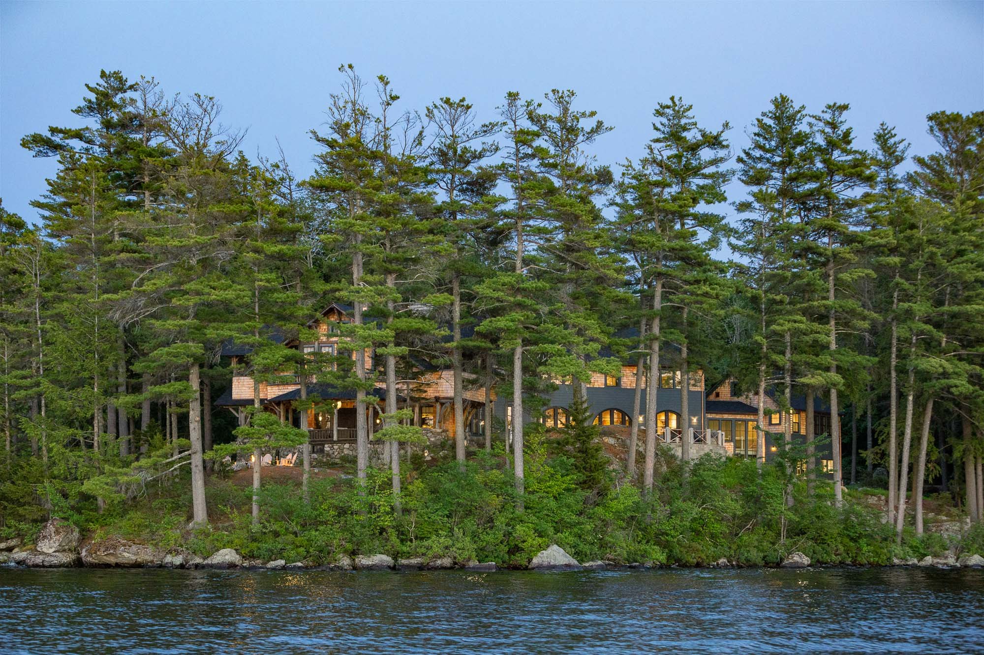 Home on Lake Sunapee with wooden exterior surrounded by green trees-Kate Maloney Interior Design