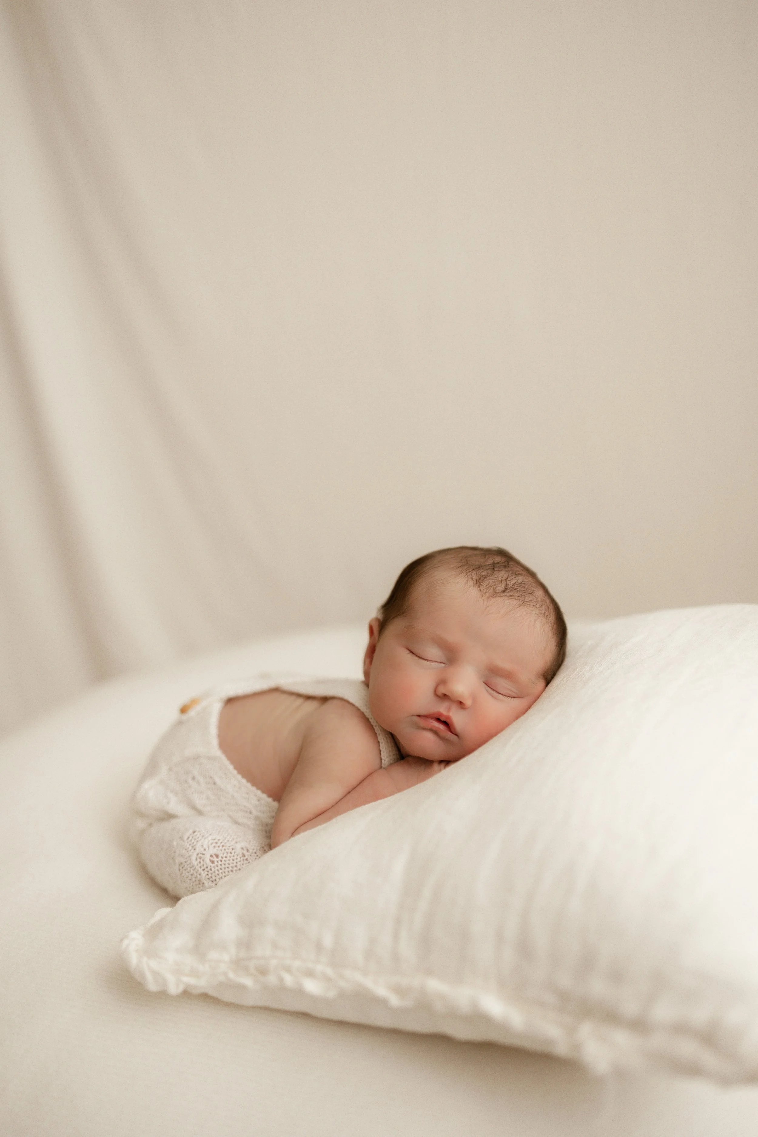 Newborn sleeping on soft cream cushion 
