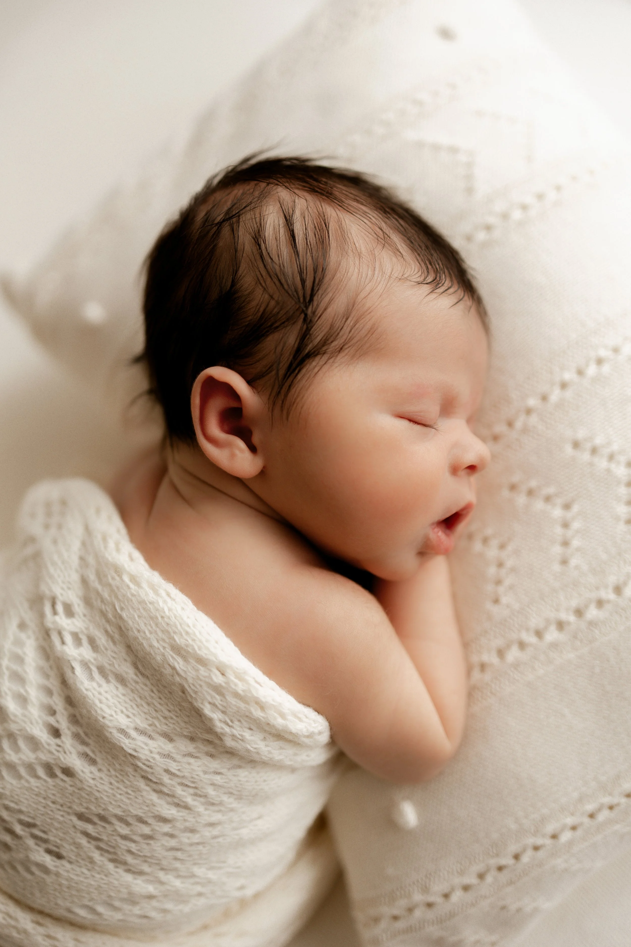 newborn baby sleeping wrapped in soft cream blanket
