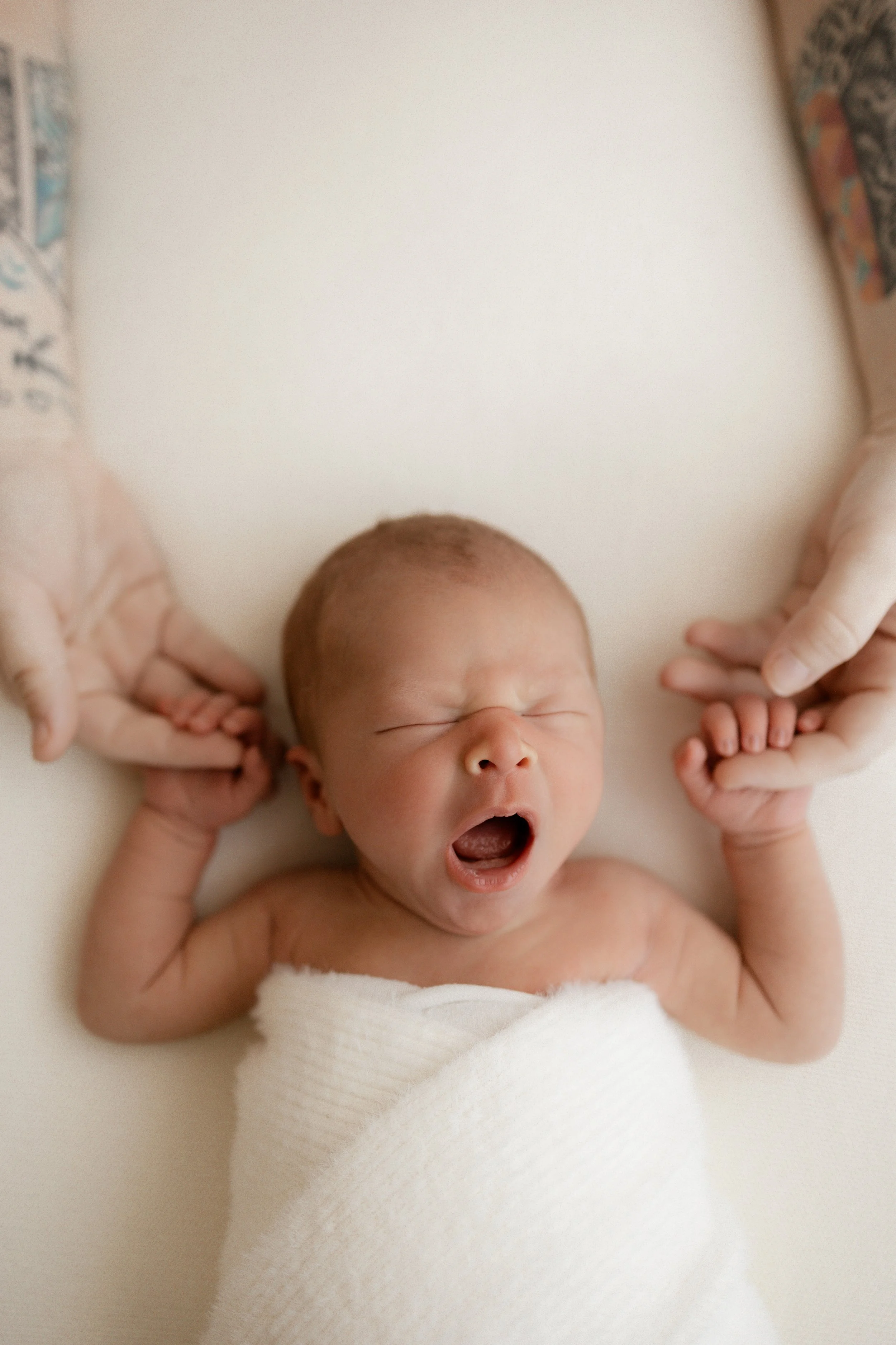 Newborn yawns holding parents hands